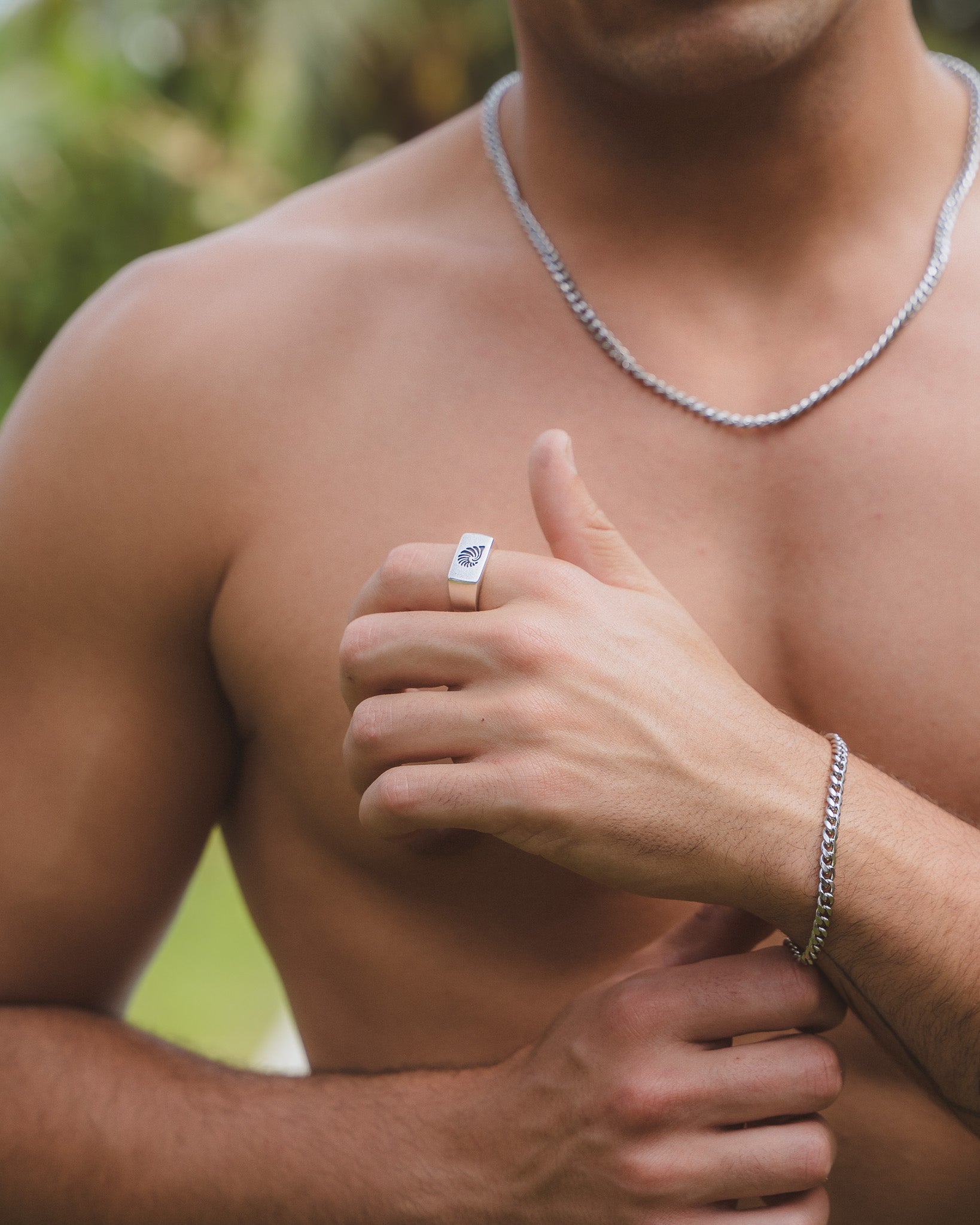 Hombre con anillo plateado de concha de cara cuadrada en el dedo y collar de cadena plateada.