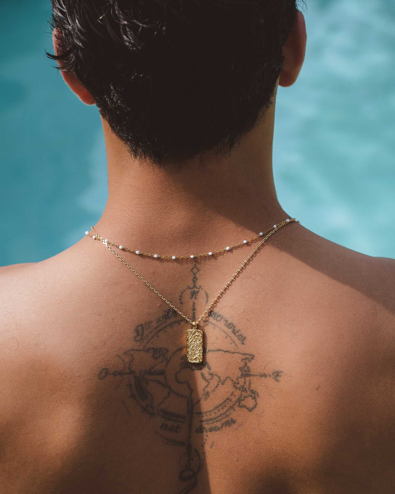 Front view of a man wearing two Moonrock gold necklaces with textured pendant and white bead accents