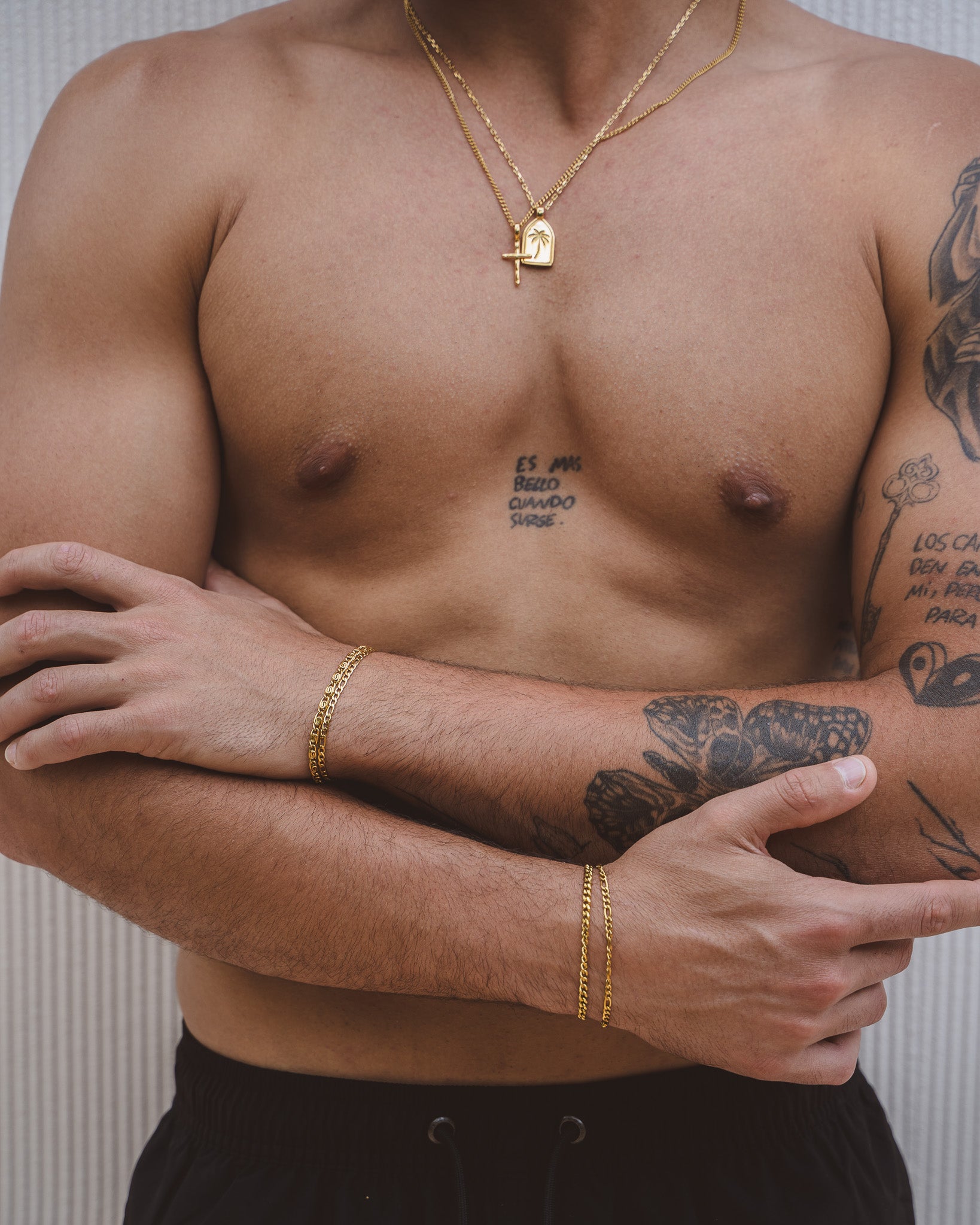 Model wearing two gold chains with a cross pendant and palm tree shield charm on the chest