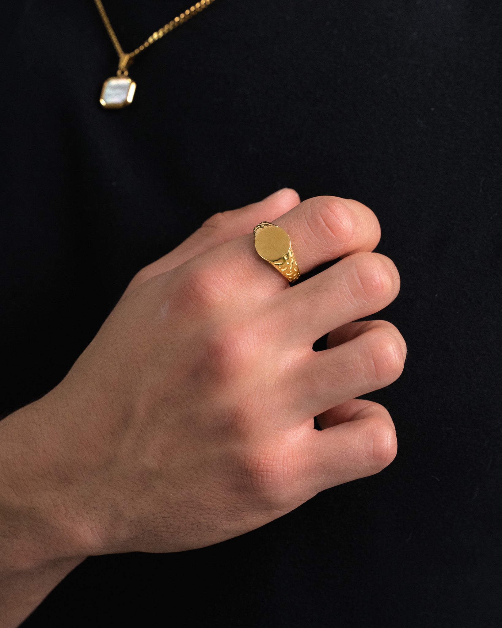 Eden gold ring with textured patterned band and blank round face held on a finger against a dark background