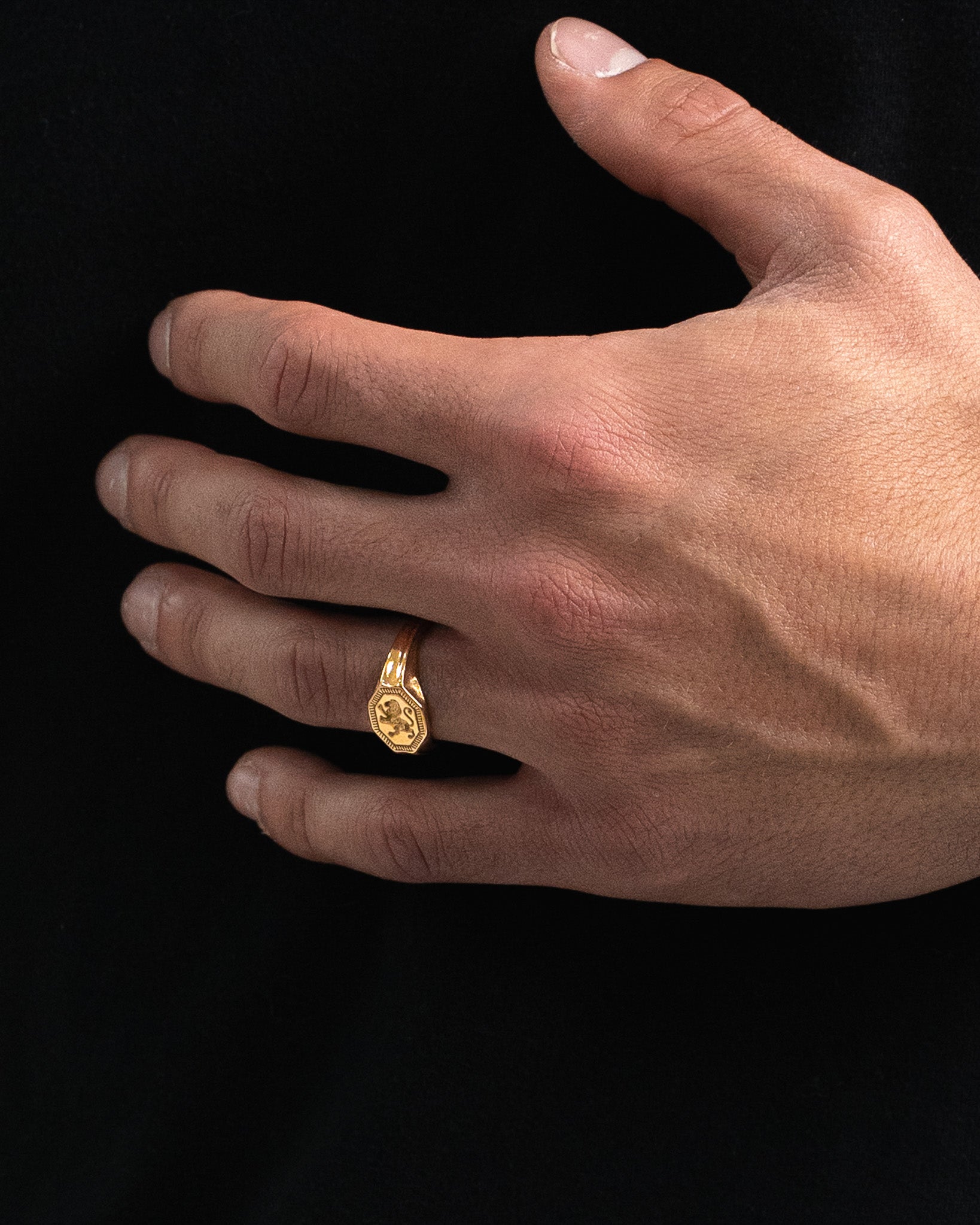 Close-up of a gold hexagonal crest ring worn on a finger against a black background