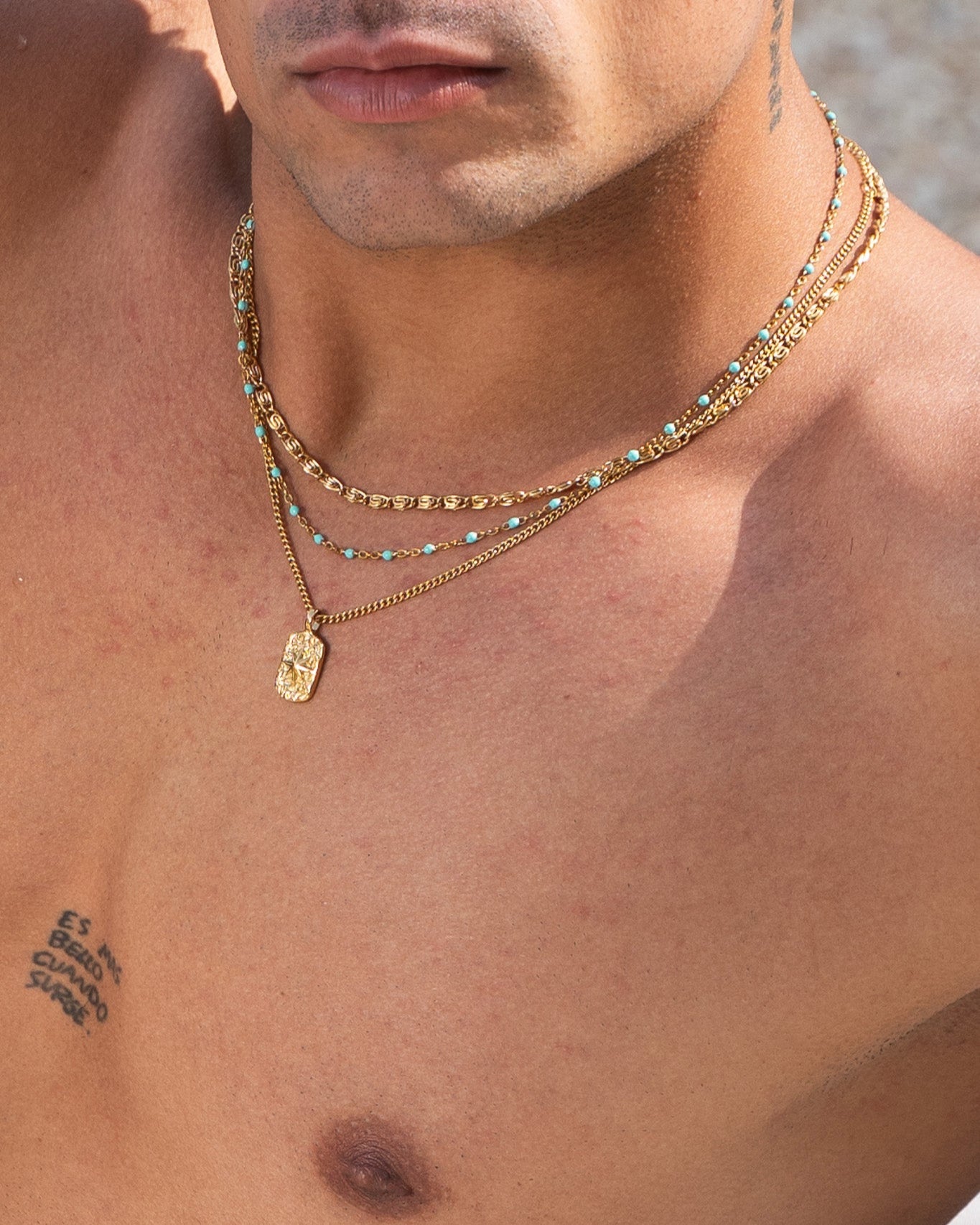 Layered gold chains with turquoise beads and a decorative rectangular pendant on the chest.