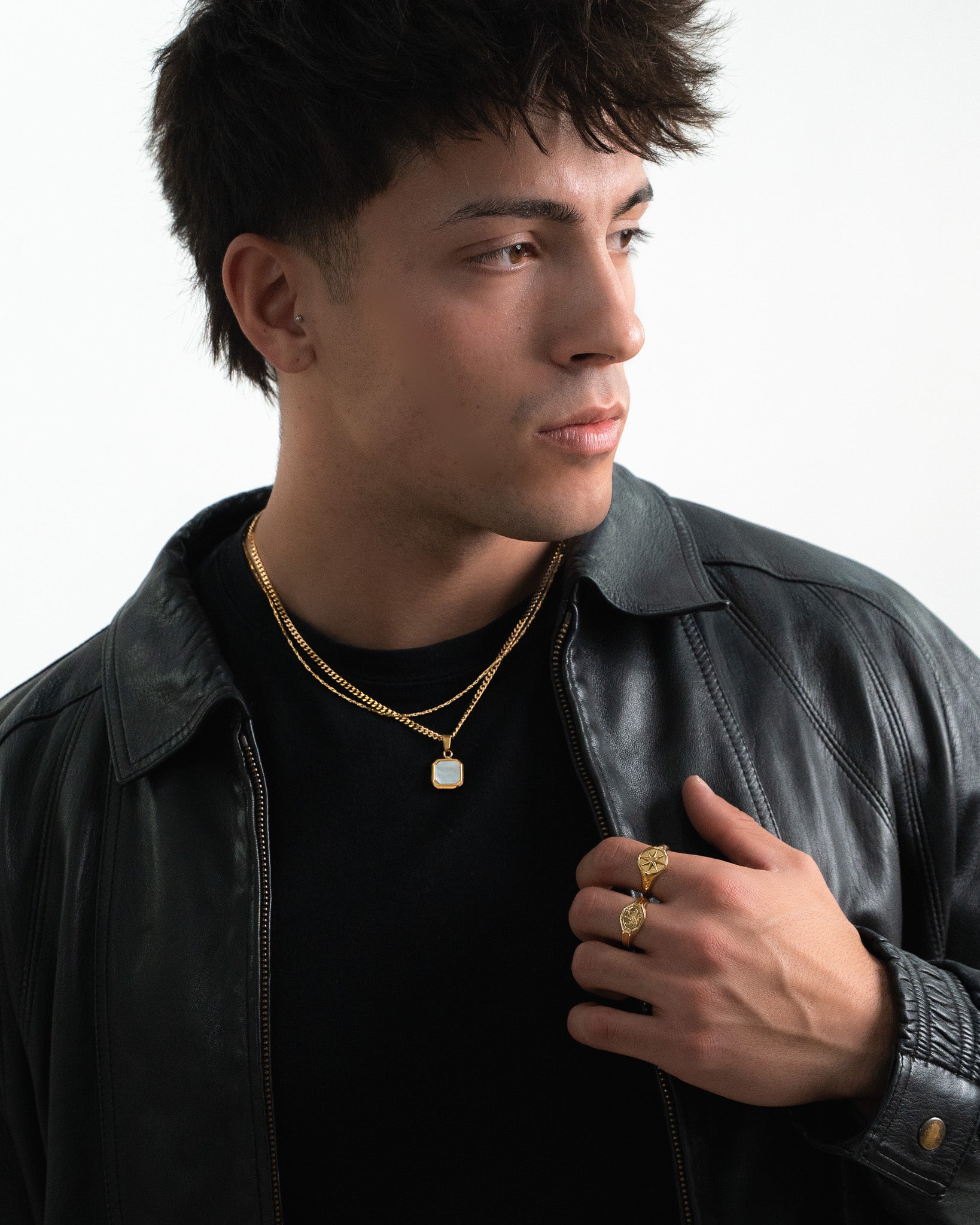 Side profile of a man wearing a NOVA GOLD necklace with a square pale pendant and a black leather jacket