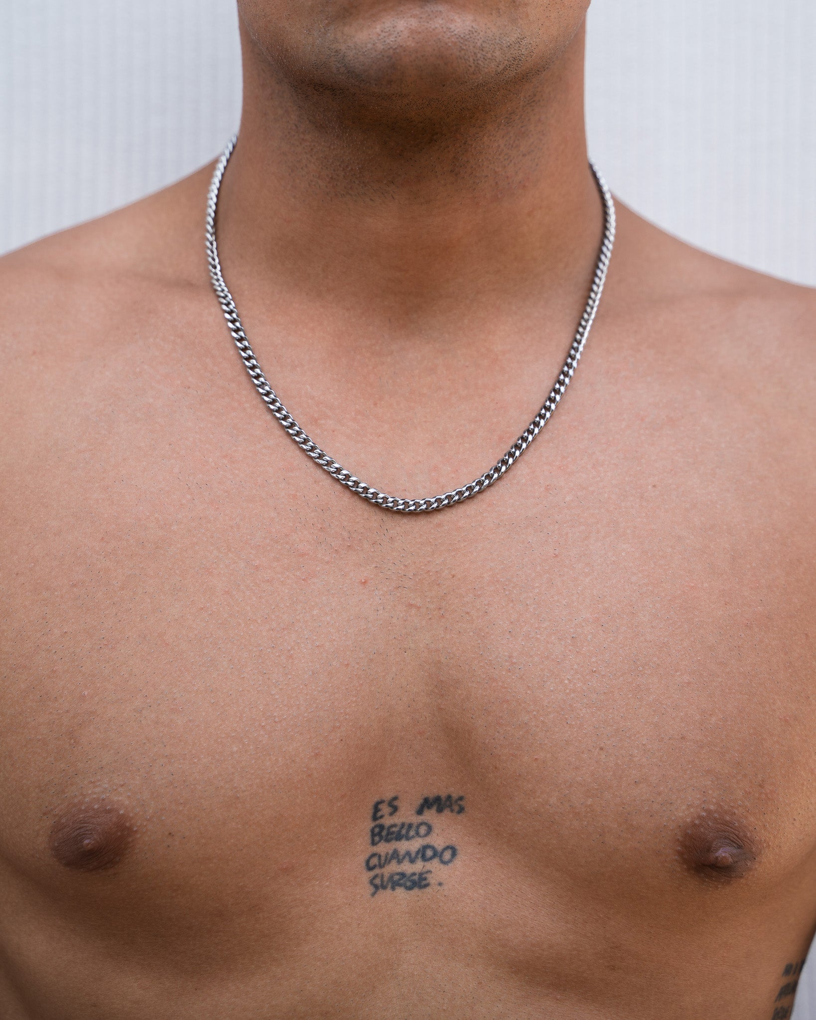 Chest shot of a man wearing a 5mm Cuban silver chain with an open shirt and tattoo on his chest.