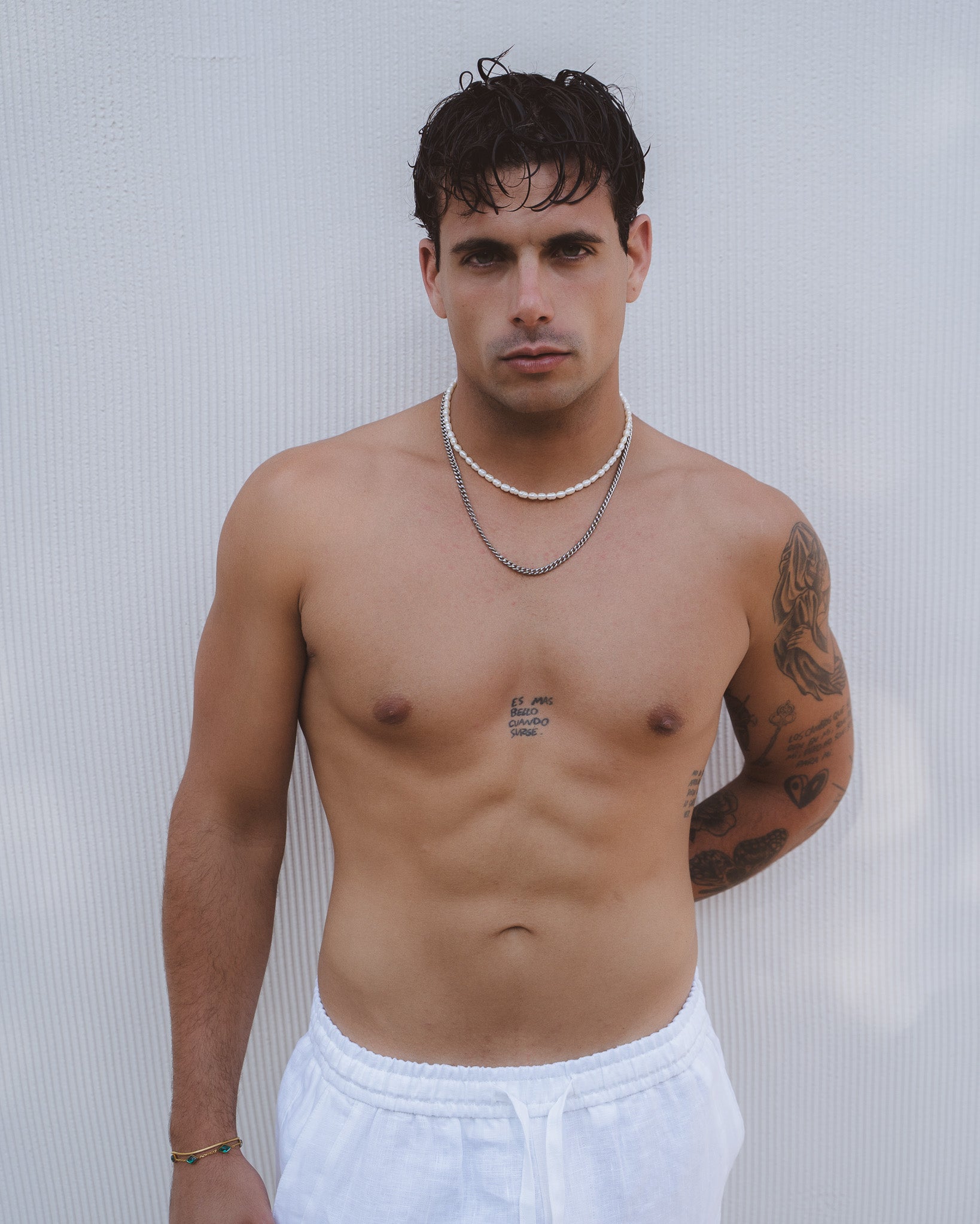 Man wearing a Belize Pearl Chain double strand white freshwater pearls with a silver chain against a pale background