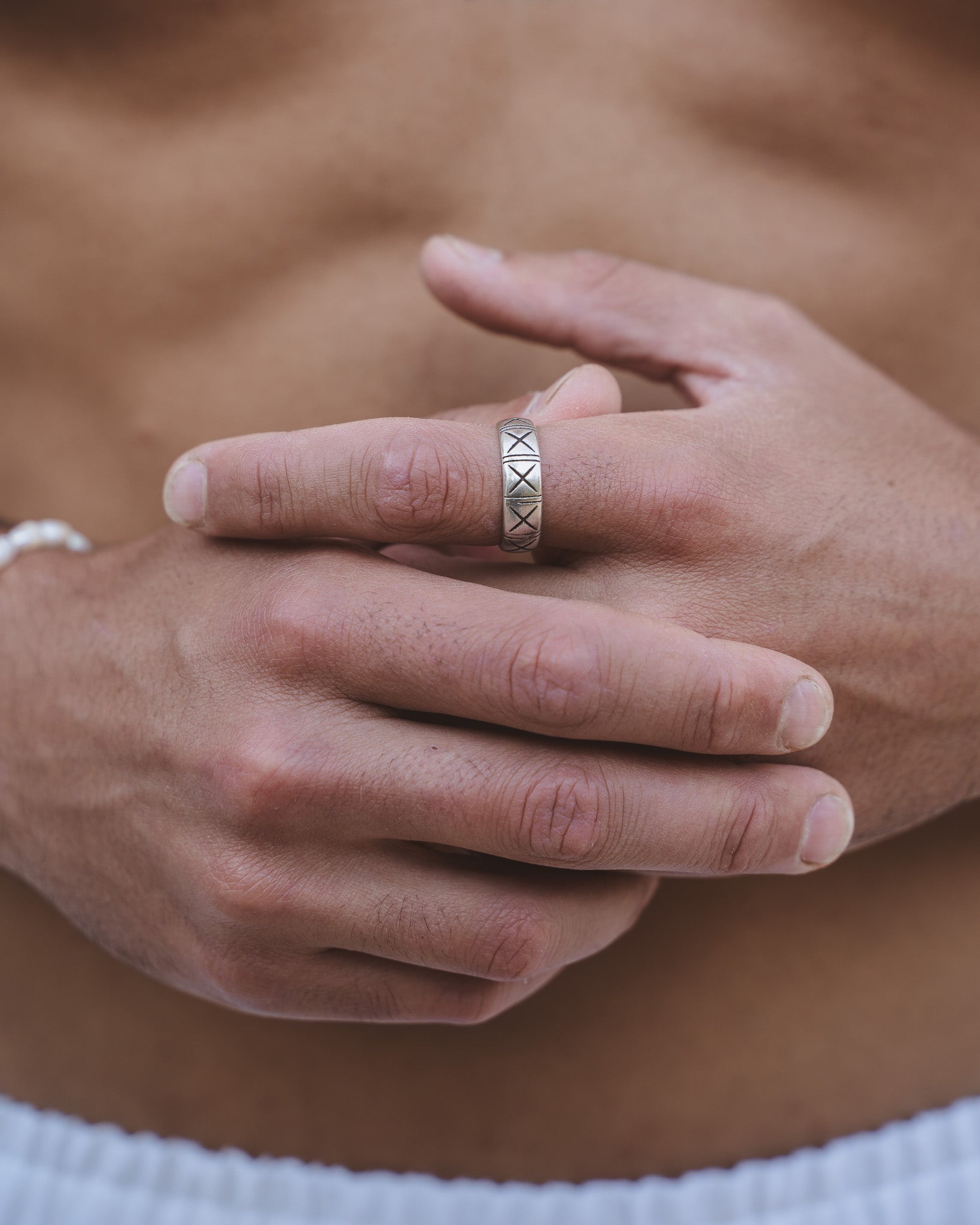 Mano con el anillo plateado TNF en el dedo y collar plateado con colgante visible sobre el pecho