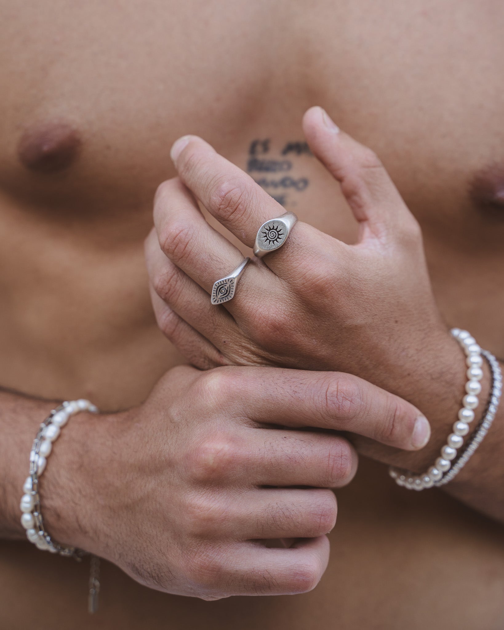 Anillo ORUS con motivo de ojo en el dedo con pulsera de perlas visible al fondo.