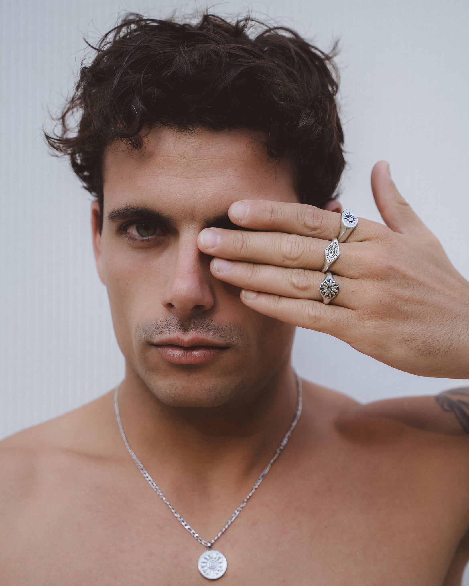 Primer plano de un hombre con varios anillos plateados con símbolos de sol y ojo en los dedos