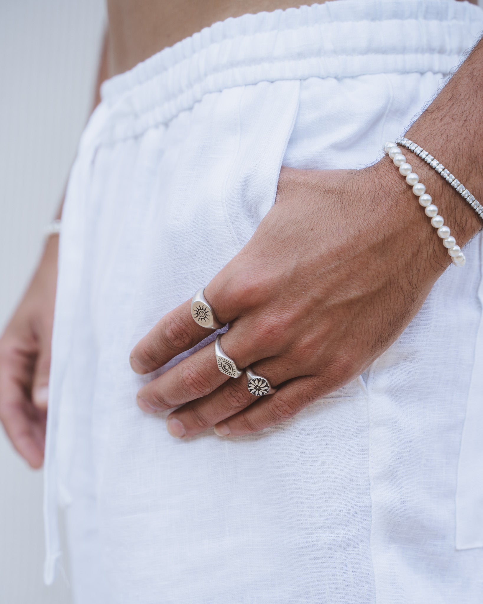 Vista lateral de un hombre con anillos plateados ENERGY, pulsera de perlas y pulsera de cristal.