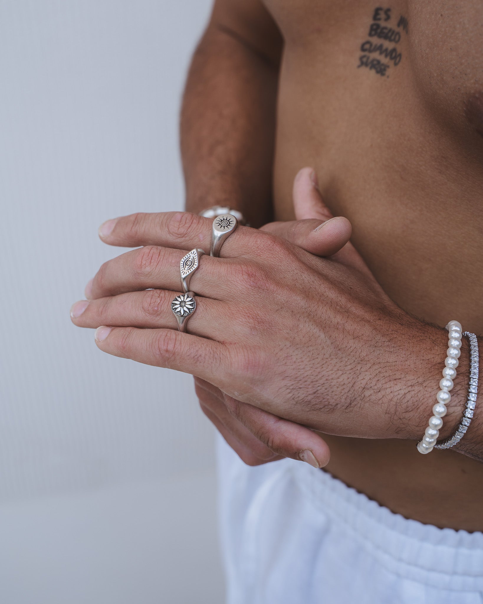 Mano de modelo con anillo plateado Fleur con motivo de sol entre anillos apilados y pulsera de perlas