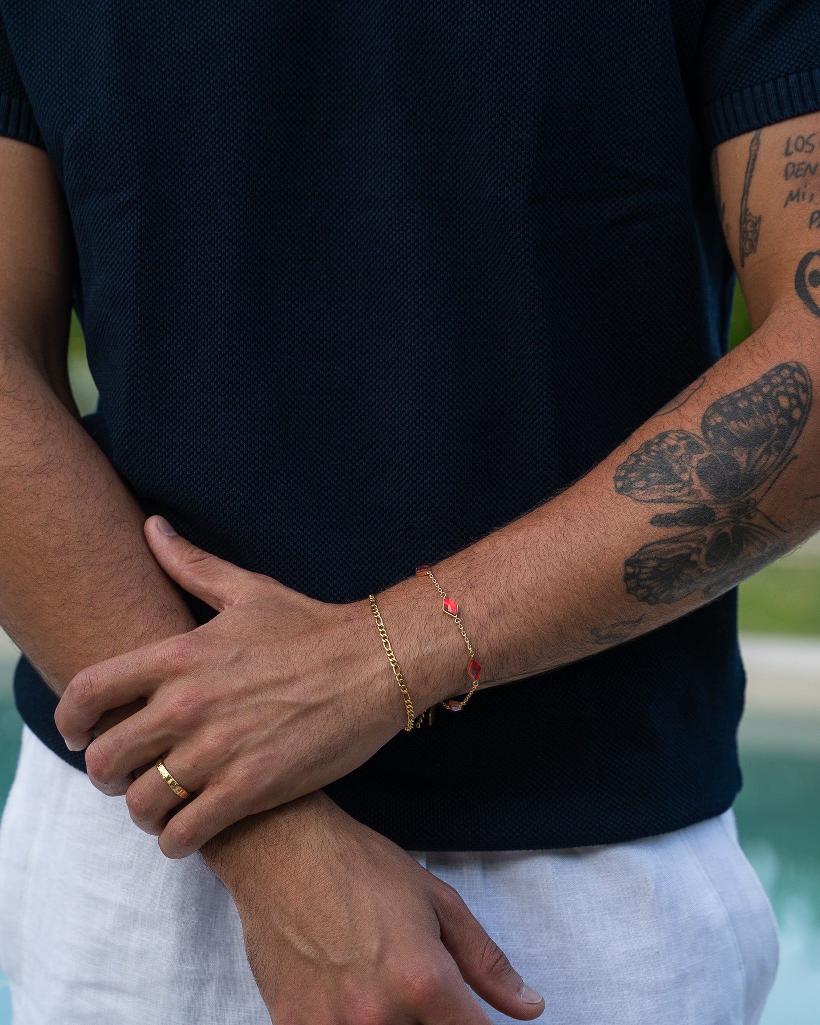 Amberes gold bracelet with red gemstone links worn on a man's wrist against a dark navy knit shirt