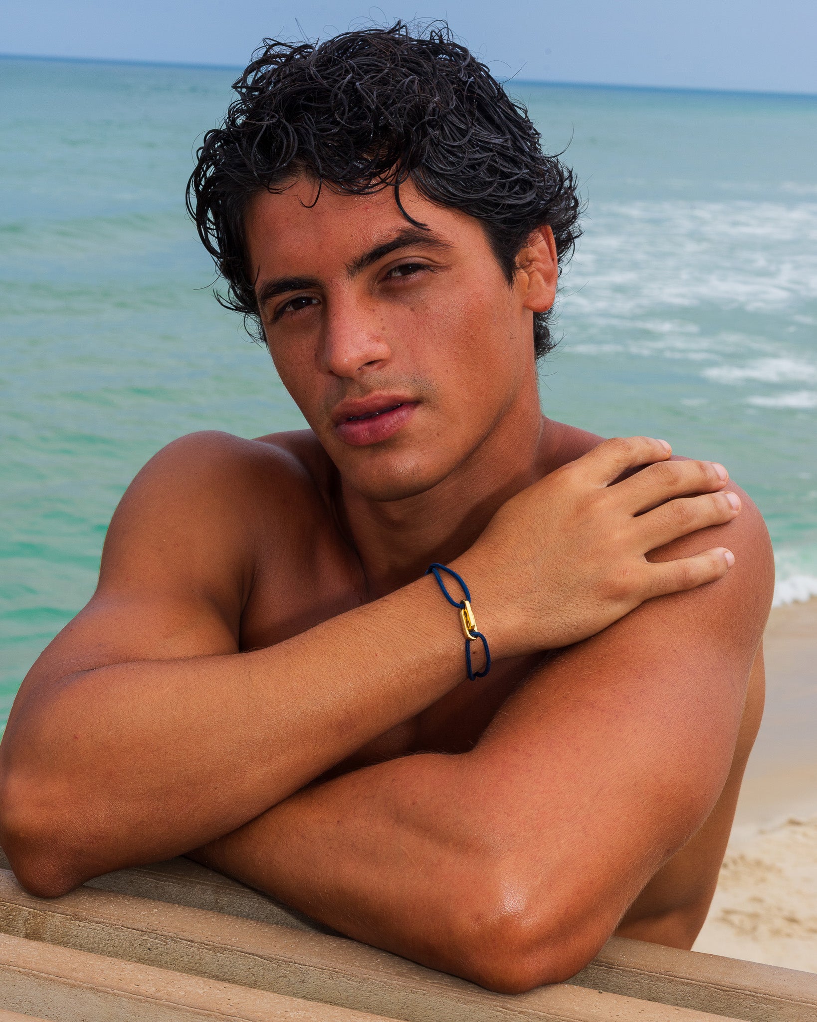 Hombre en la playa con la pulsera ATLANTIS de oro en la muñeca