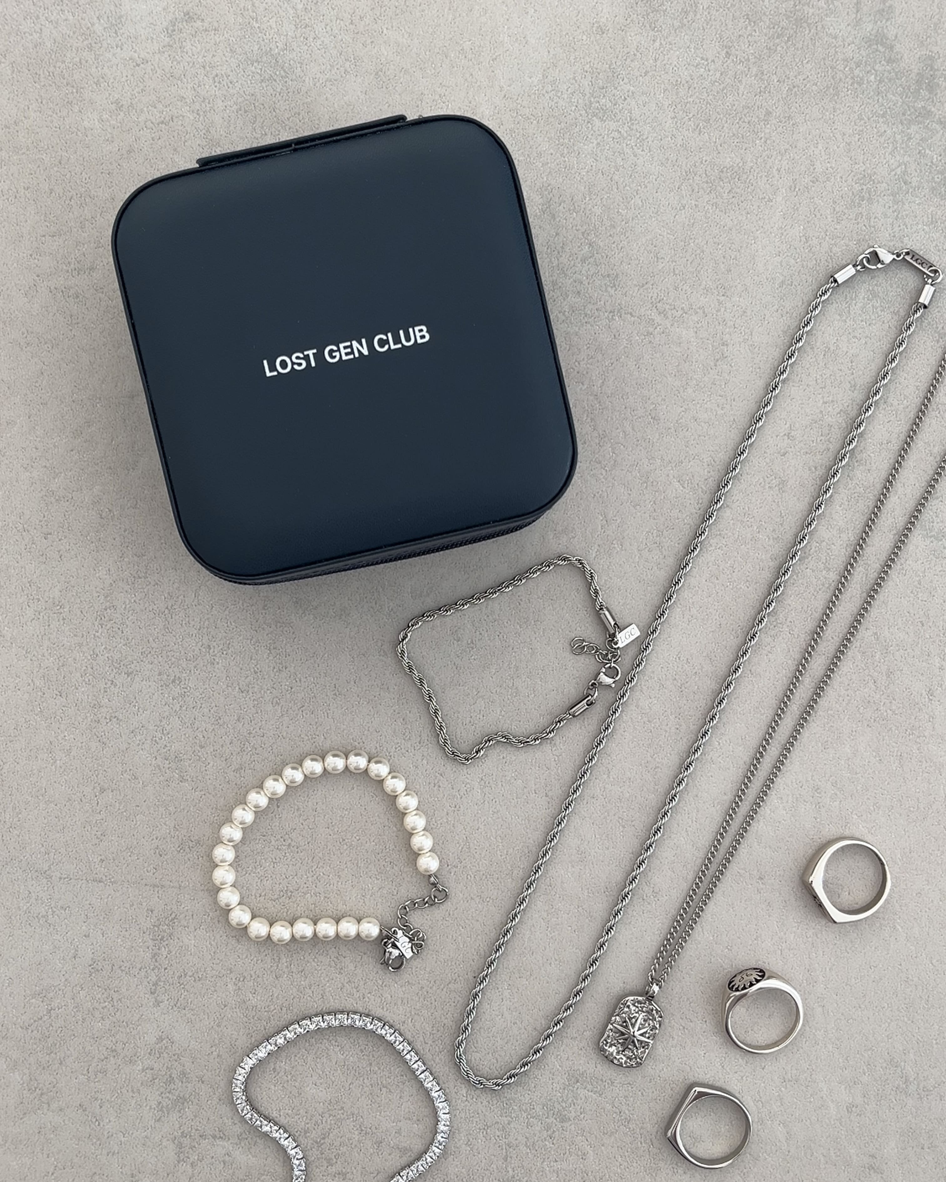Navy travel jewelry case on a gray surface with silver chains nearby and the LOST GEN CLUB logo visible