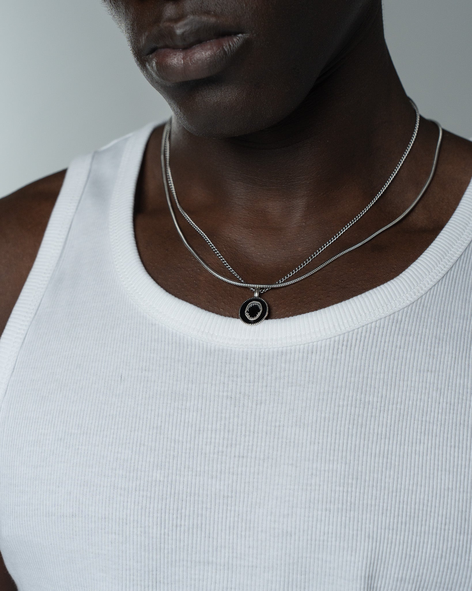 Two silver Sunset Chains rest on a man’s chest over a white tank top.