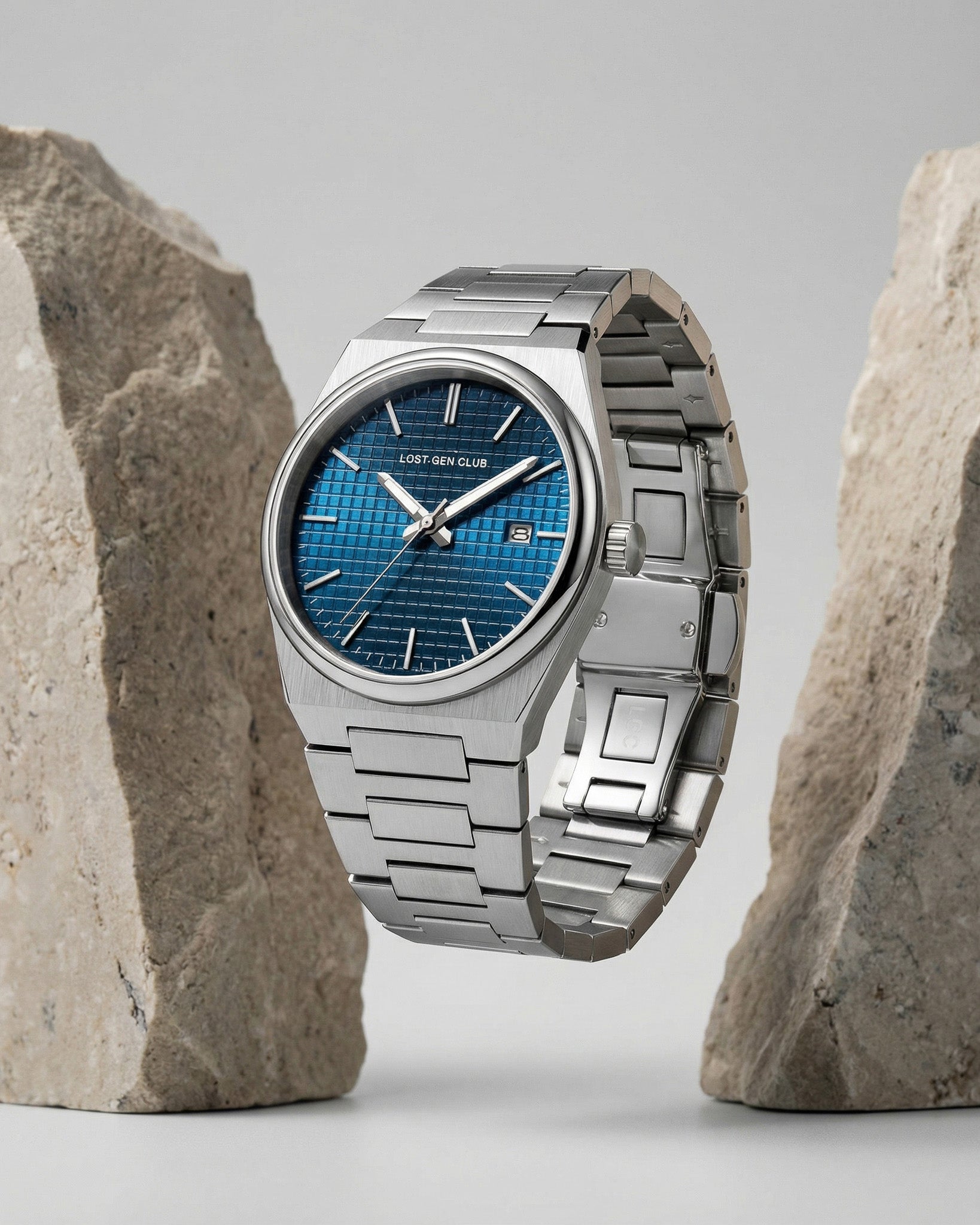 AUREN watch with blue dial and stainless steel bracelet displayed against a rocky backdrop.