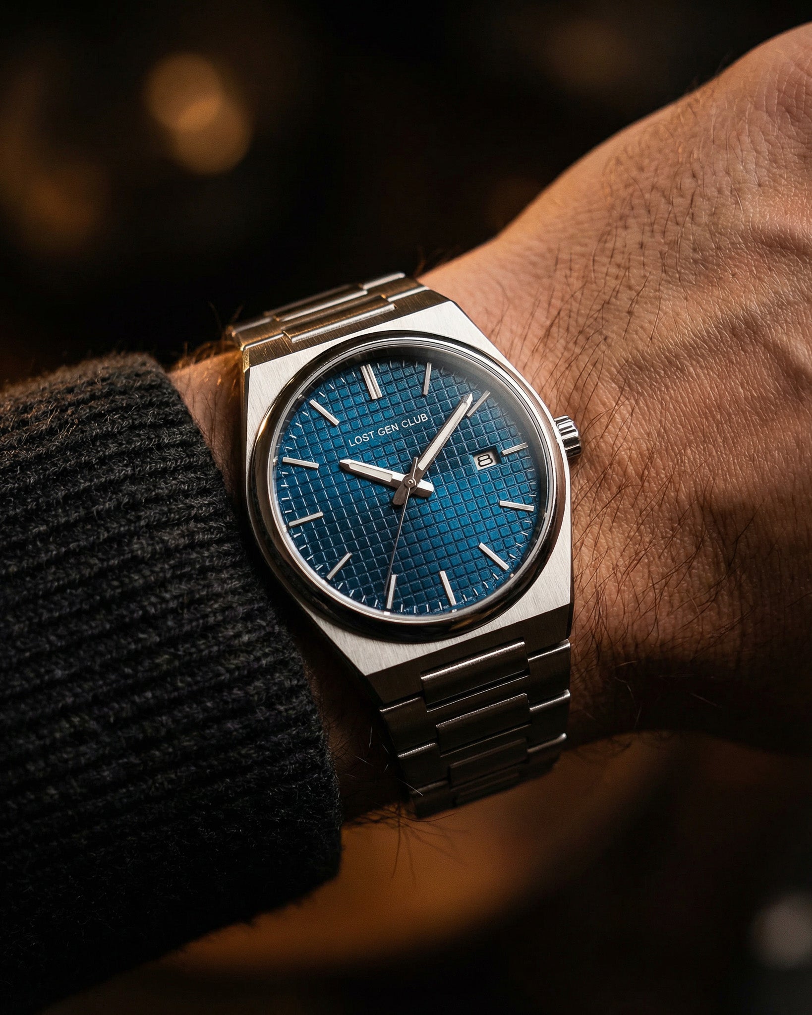 AUREN watch on the wrist with a blue dial and silver stainless steel band in warm lighting.