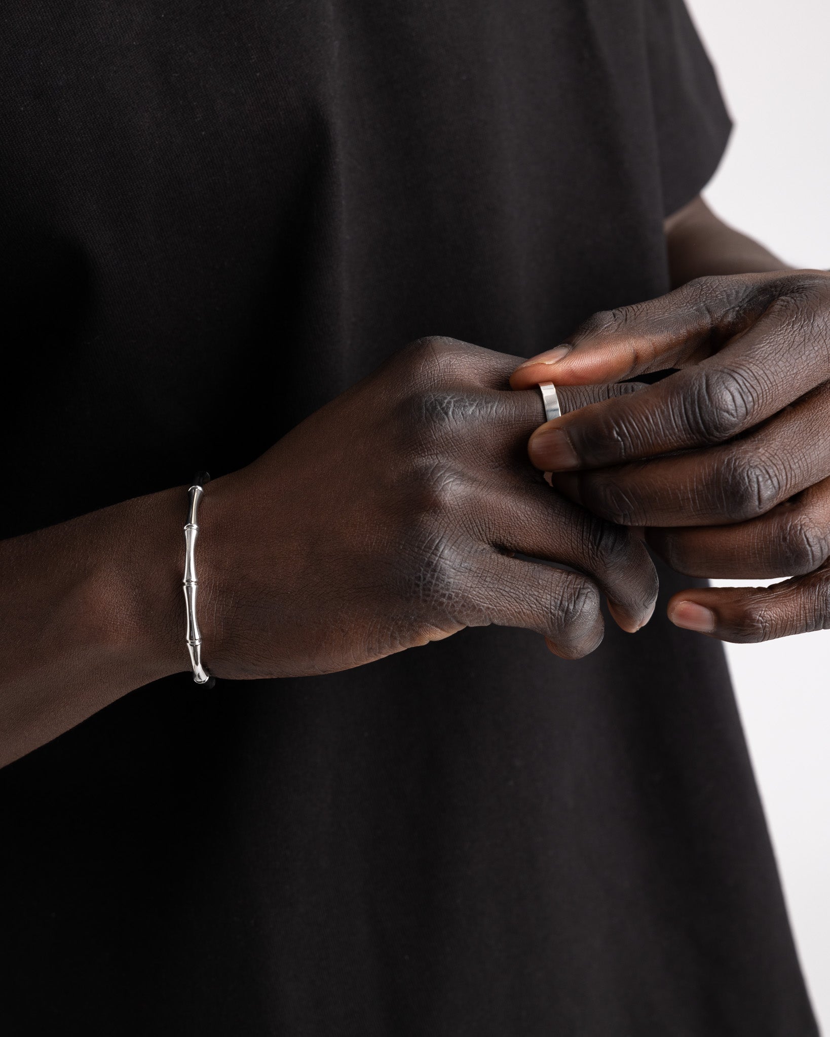 Primer plano de una mano de piel oscura con anillo plateado fino y pulsera visible en la muñeca