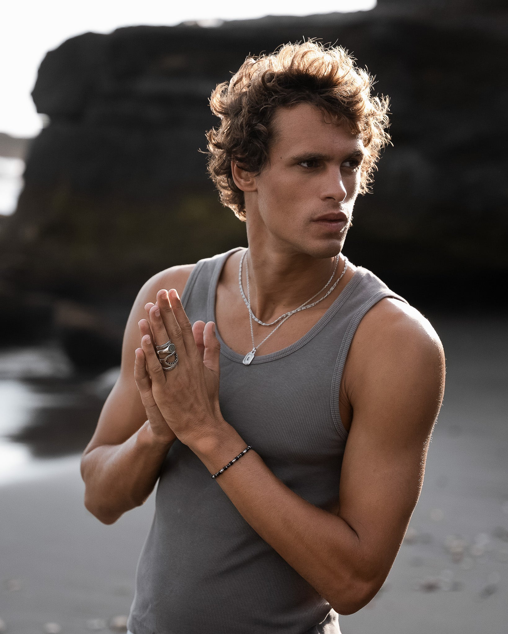 Close up of a man wearing a black agate stone bracelet with gold spacers and a silver necklace