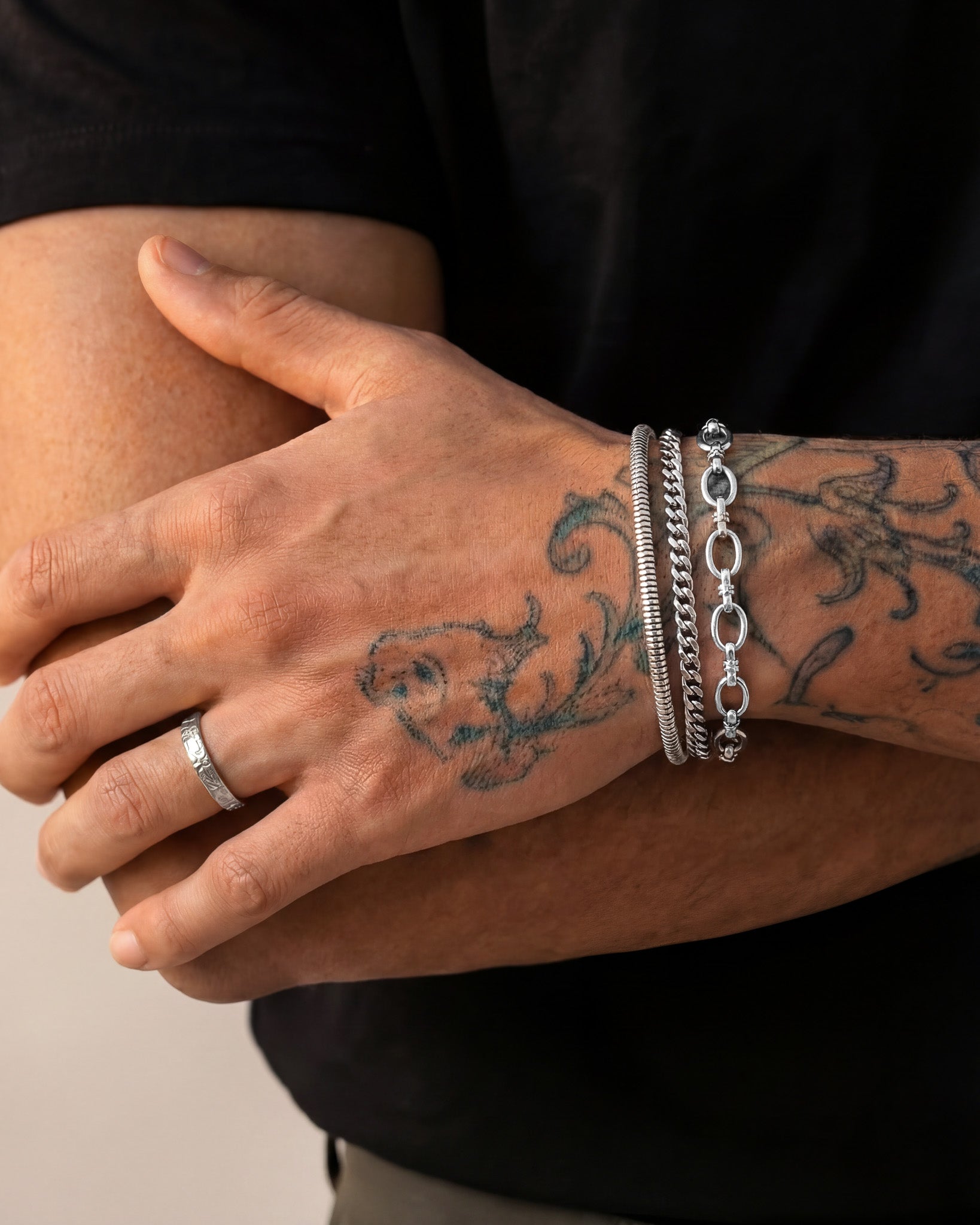 Stacked silver Cuban link bracelets on the wrist with a visible tattooed arm