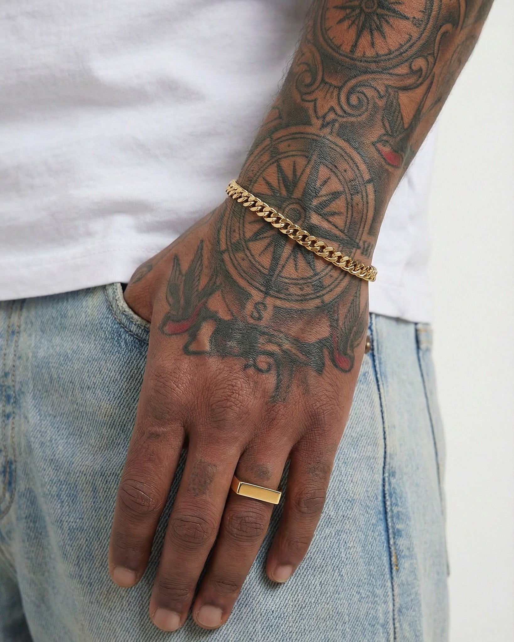 Gold Milo ring with a wide flat top on the middle finger, paired with a gold chain bracelet.
