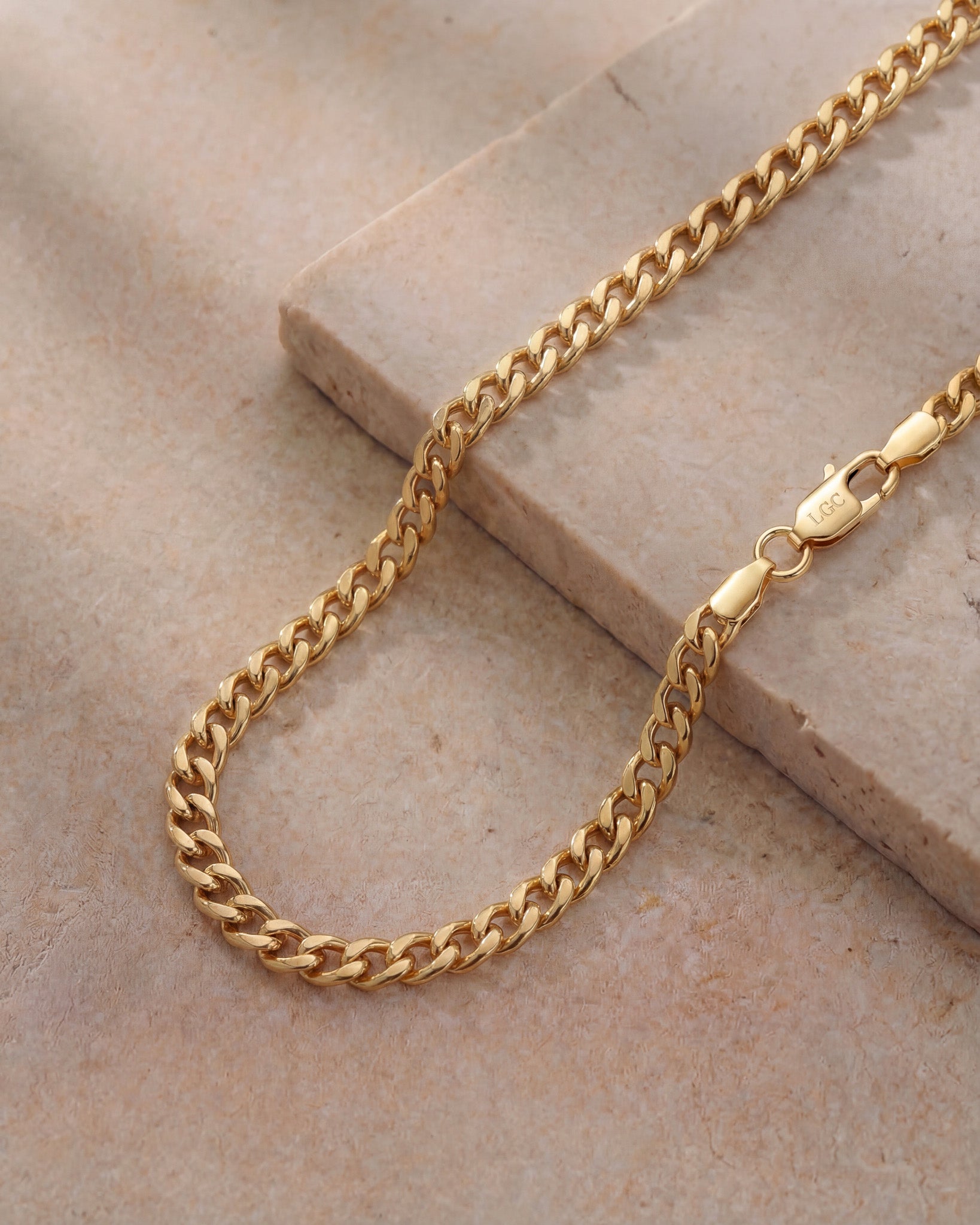 Close up of a 5mm Cuban gold chain with a lobster clasp on a stone surface