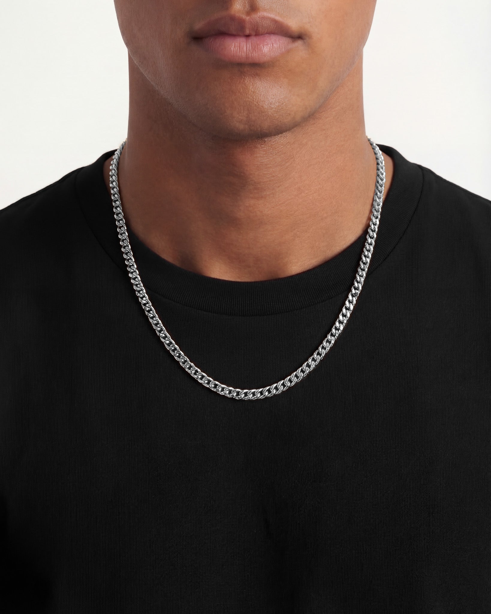 Close-up of a man wearing a 5mm Cuban silver chain around his neck over a black shirt.