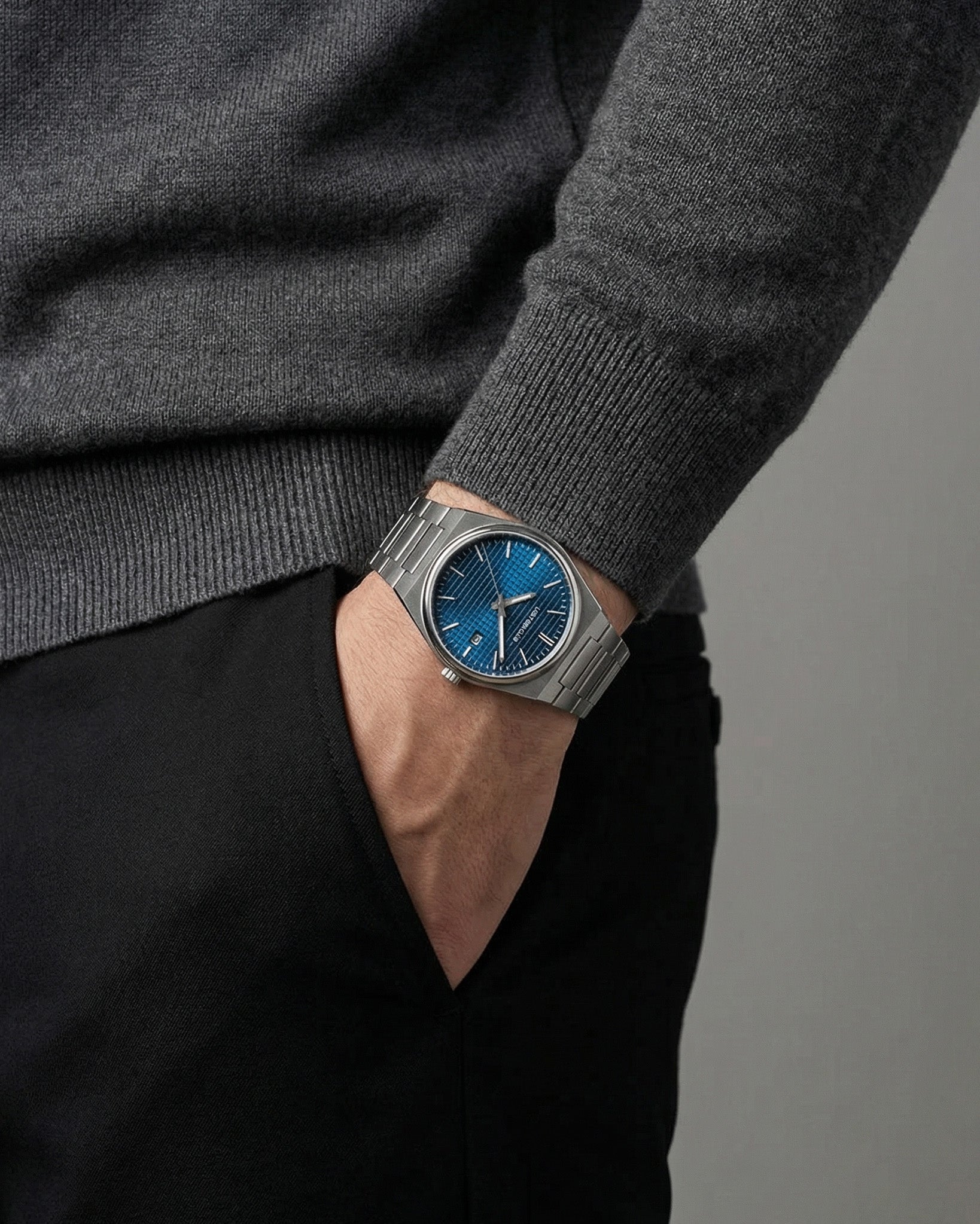 AUREN watch with a textured blue dial and stainless steel bracelet on a gray knit sleeve.