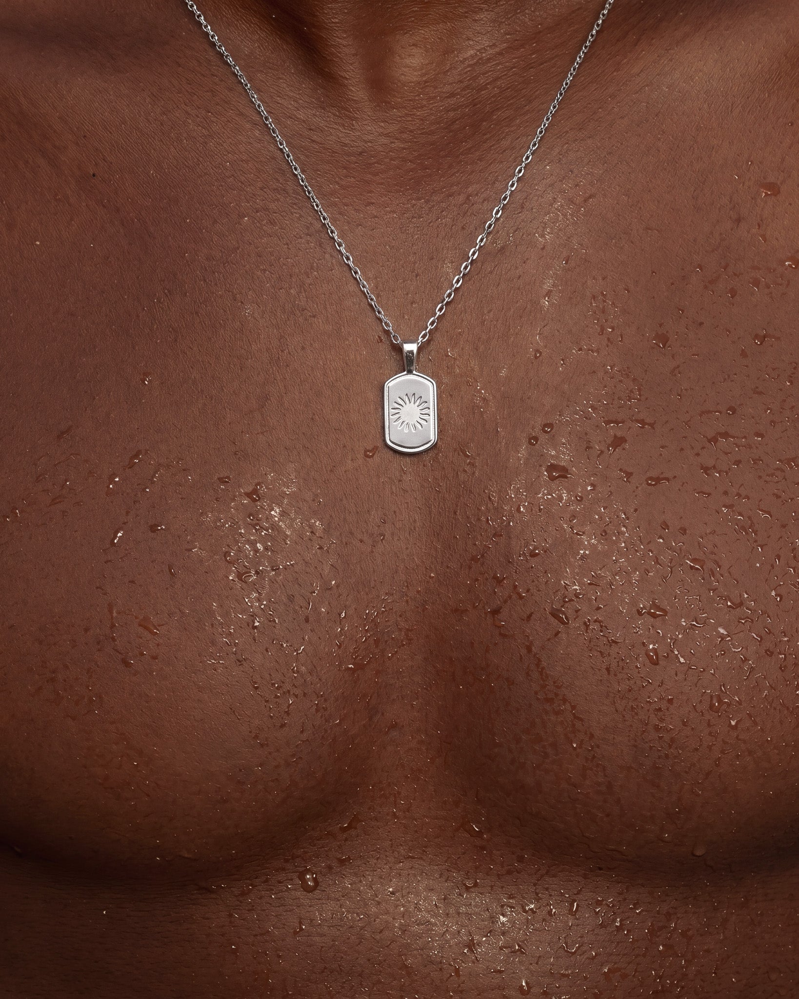 Silver DAYSTAR necklace resting on dark skin featuring a rounded rectangular sunburst pendant