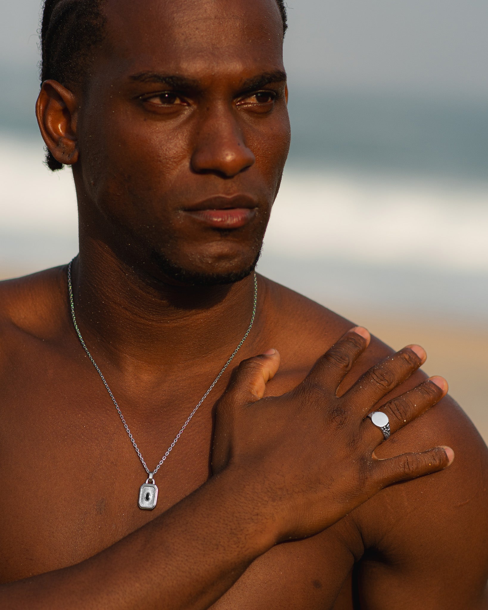 Primer plano de un hombre con anillo plateado EDEN de cara redonda en el dedo anular, collar visible.