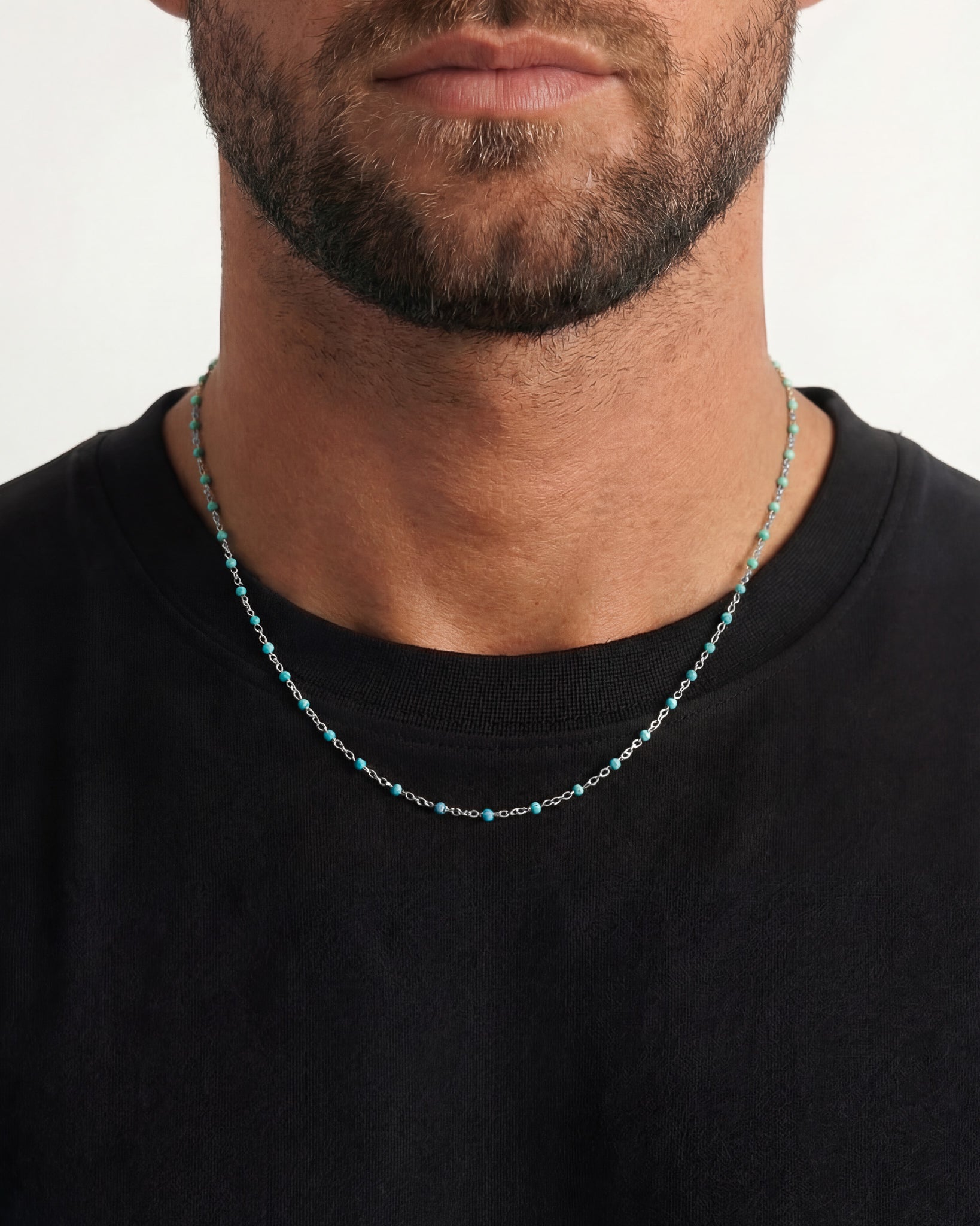 Close-up of a silver chain necklace with turquoise beads worn on a man’s neck over a black shirt