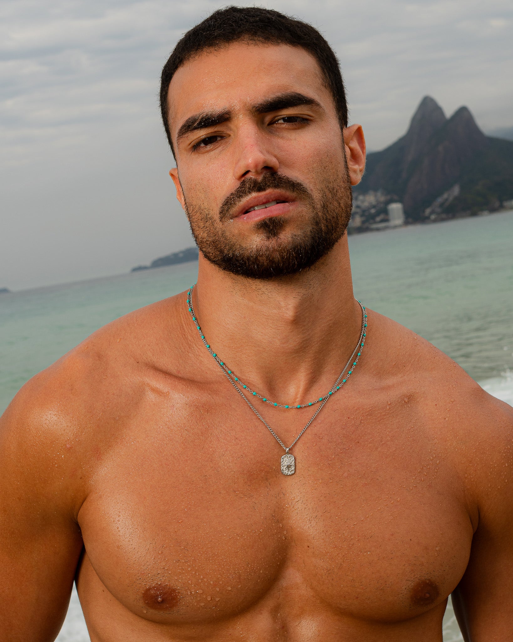 GEM Silver Chain necklace with turquoise beads worn by a man at the beach, multiple strands visible around the neck