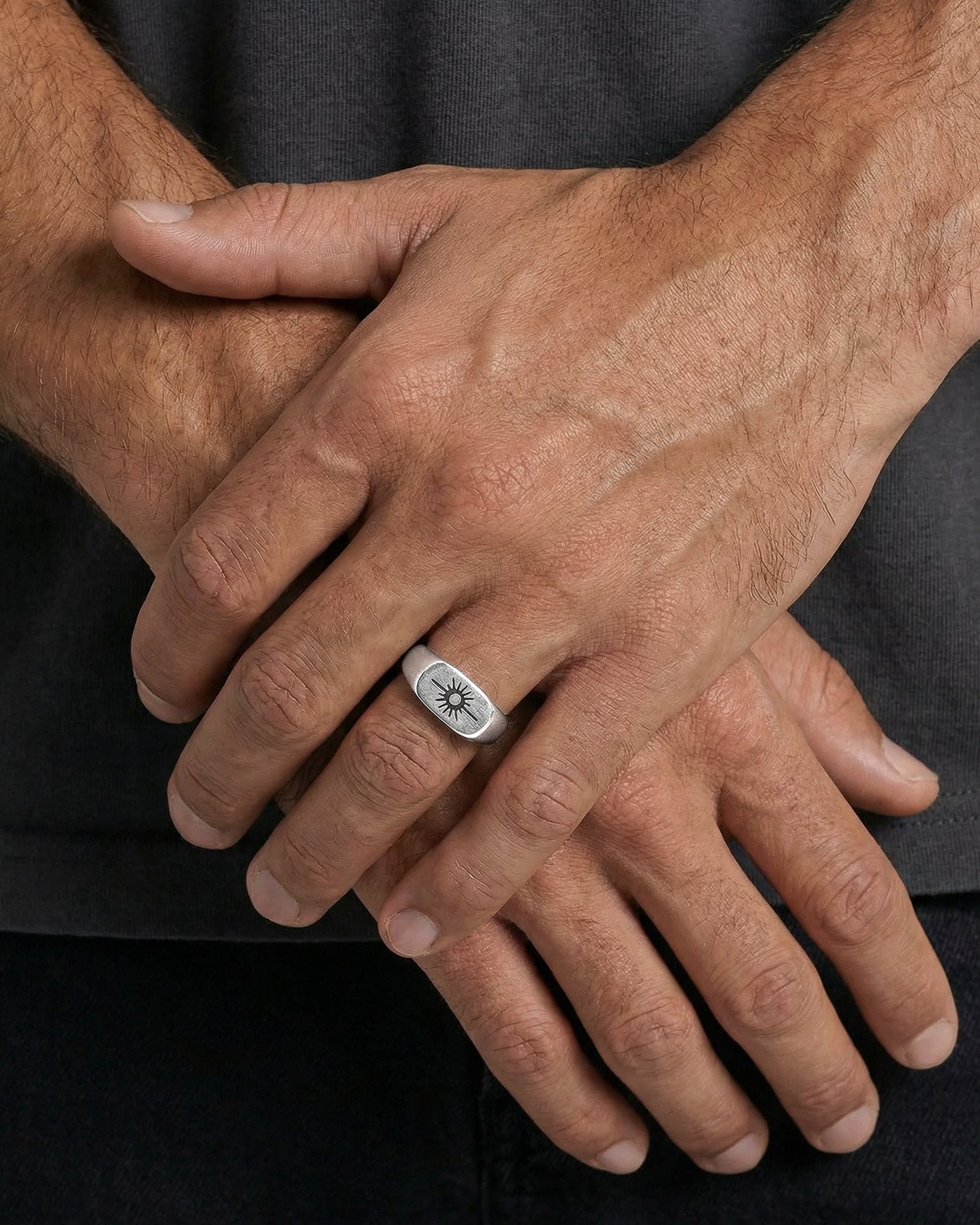 Hand wearing Horizon Silver Ring with sunburst motif and a silver chain bracelet