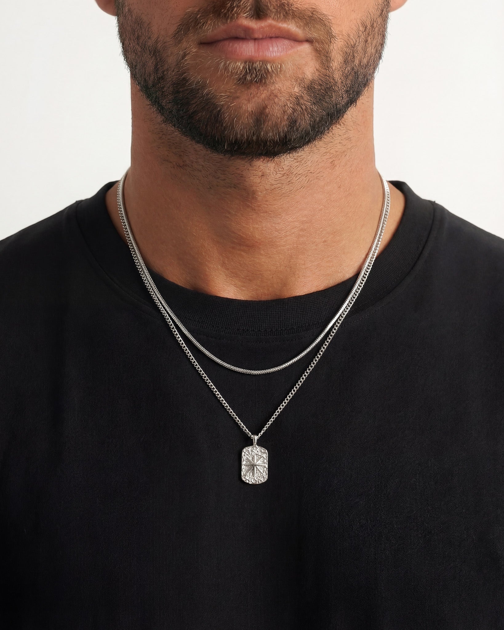 Close up of a man’s neck with layered silver chains and a pendant.