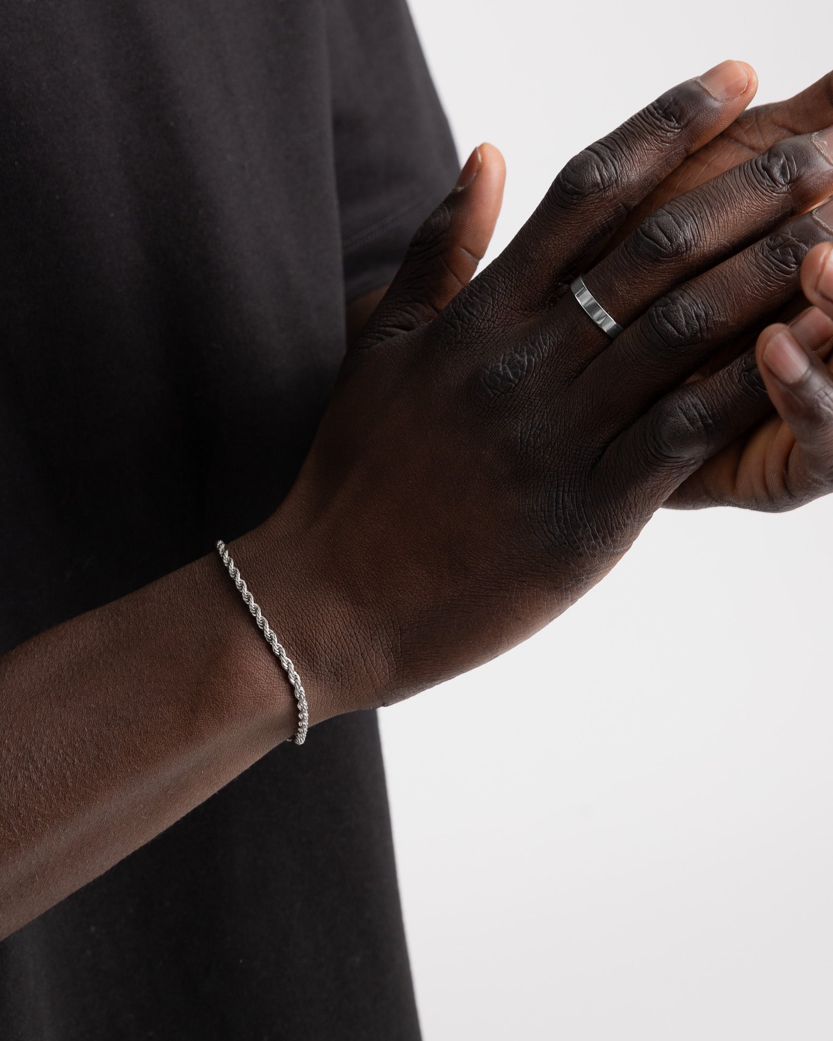 Primer plano de una mano de piel oscura con el anillo plateado VERO en el dedo y pulsera de cadena plateada en la muñeca