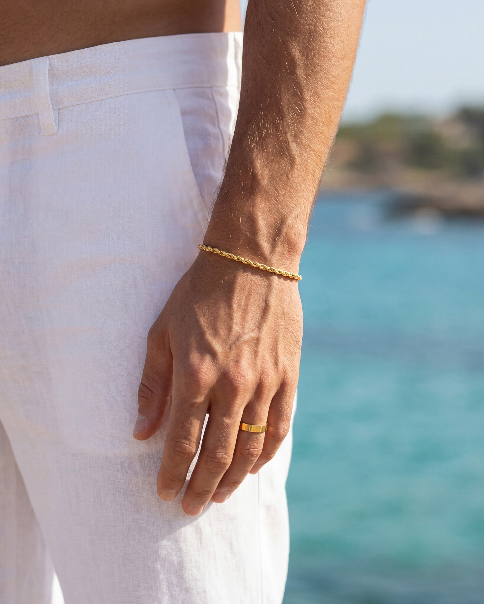 Lazio gold rope chain bracelet on the wrist with white shorts and a seaside backdrop