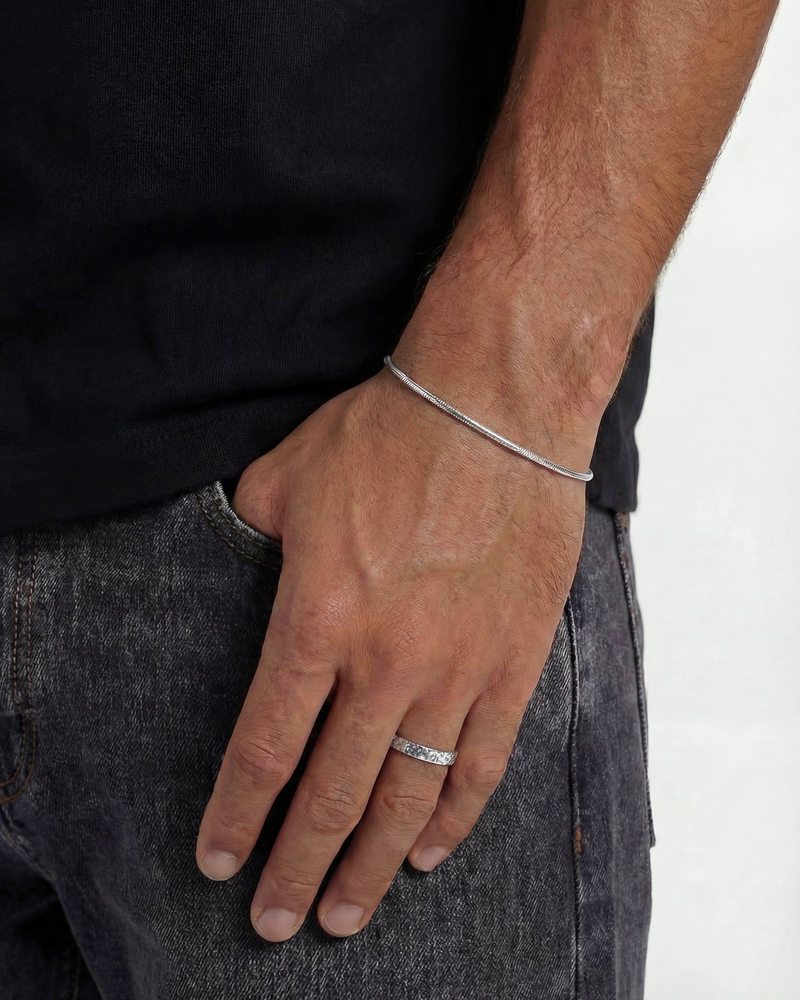 Hombre con anillo plateado martillado en el dedo con collar de colgante visible.