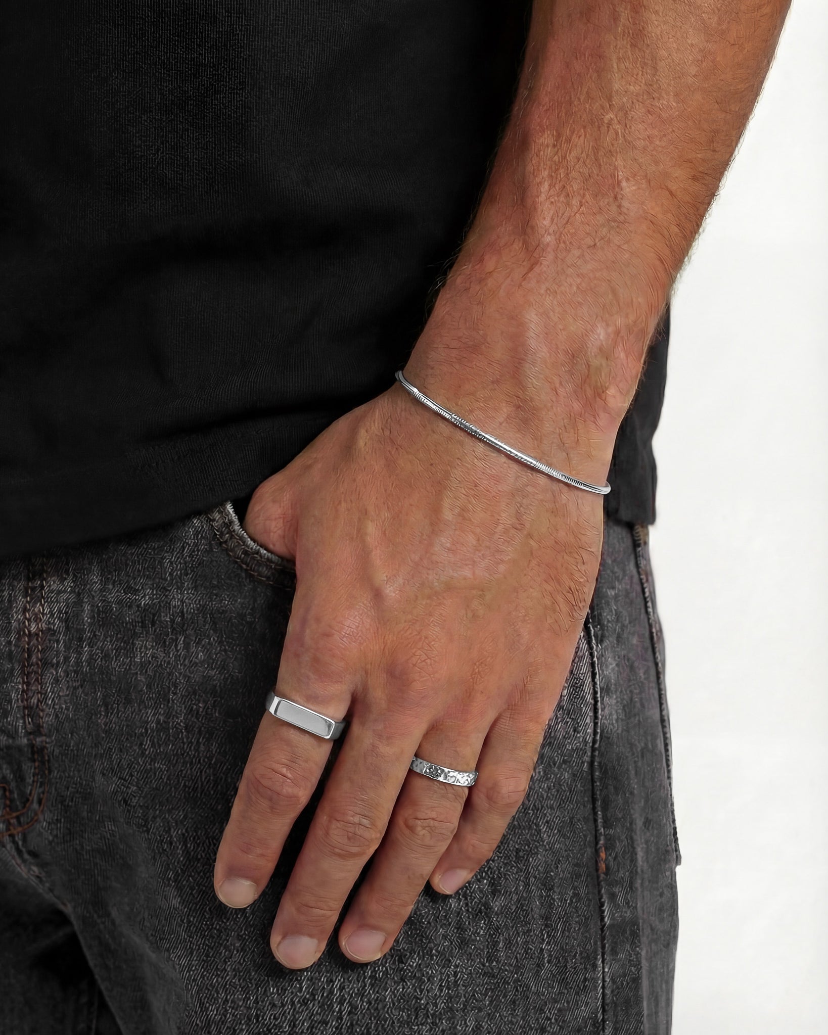 Anillos plateados MILO en la mano de un hombre con una banda fina texturizada y una banda lisa curvada
