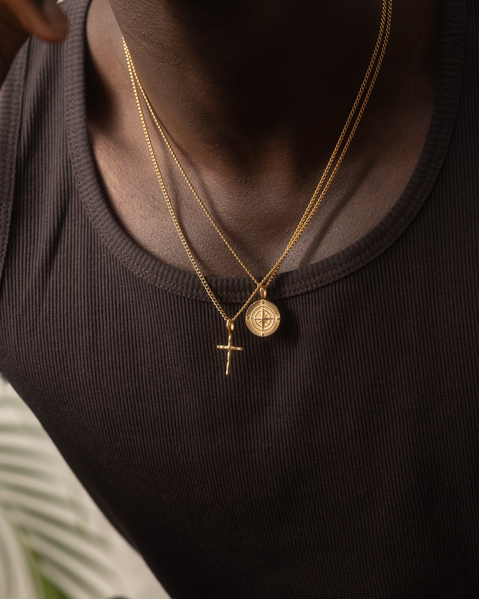 Close-up of a NORTHWALK gold necklace with a compass pendant resting on a dark knit top.