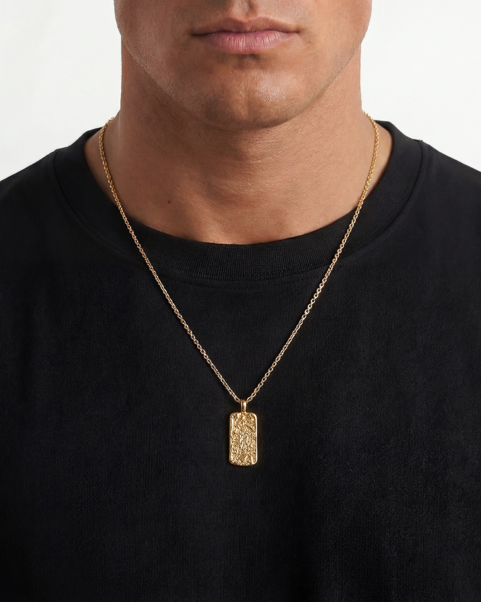 Front view of Moonrock gold necklace with hammered rectangular pendant resting on the chest against a black shirt