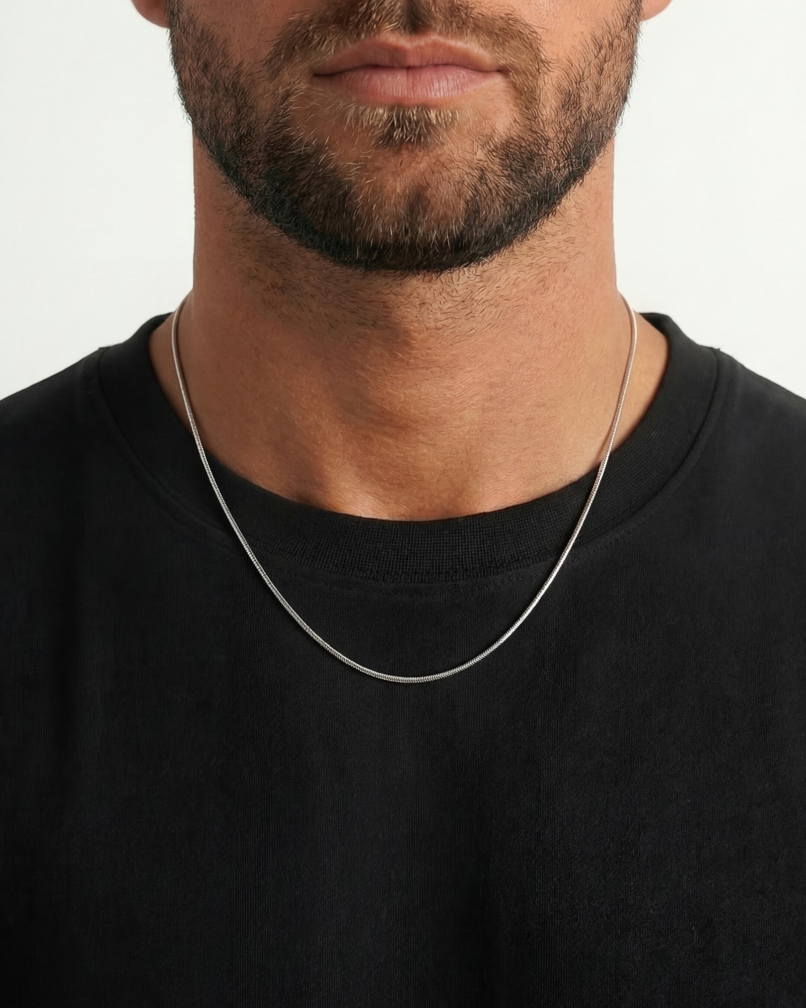 Close up of a man wearing two silver chain necklaces around the neck with a pendant