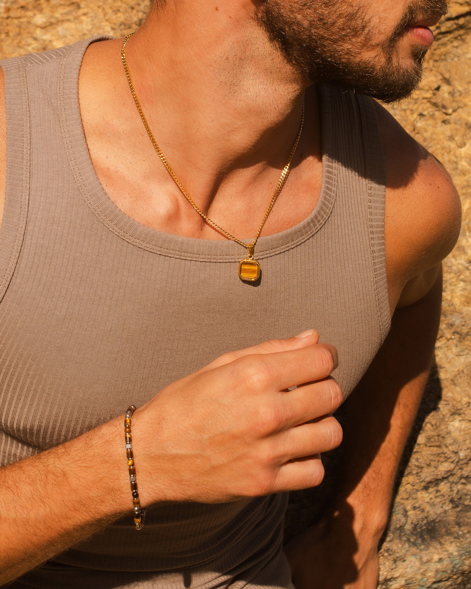Gold chain necklace with square tiger's eye pendant resting on the chest