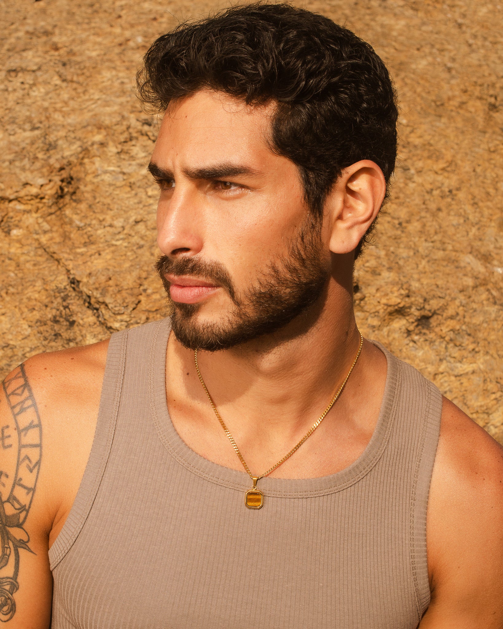 Perfil lateral de un hombre con collar dorado Nova fino sobre fondo rocoso