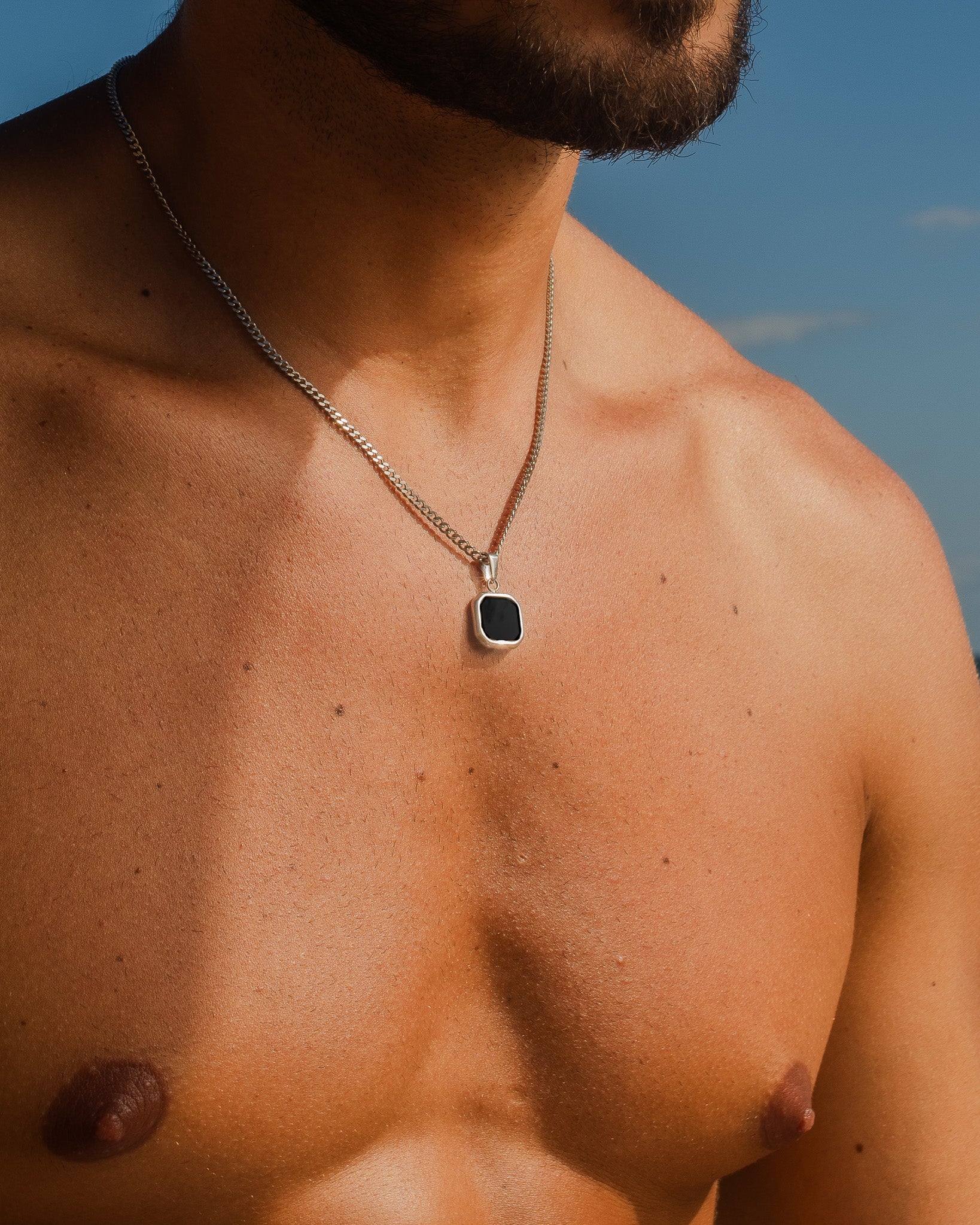Cadena del collar plateado Nova sobre el pecho descubierto de un hombre contra un cielo azul