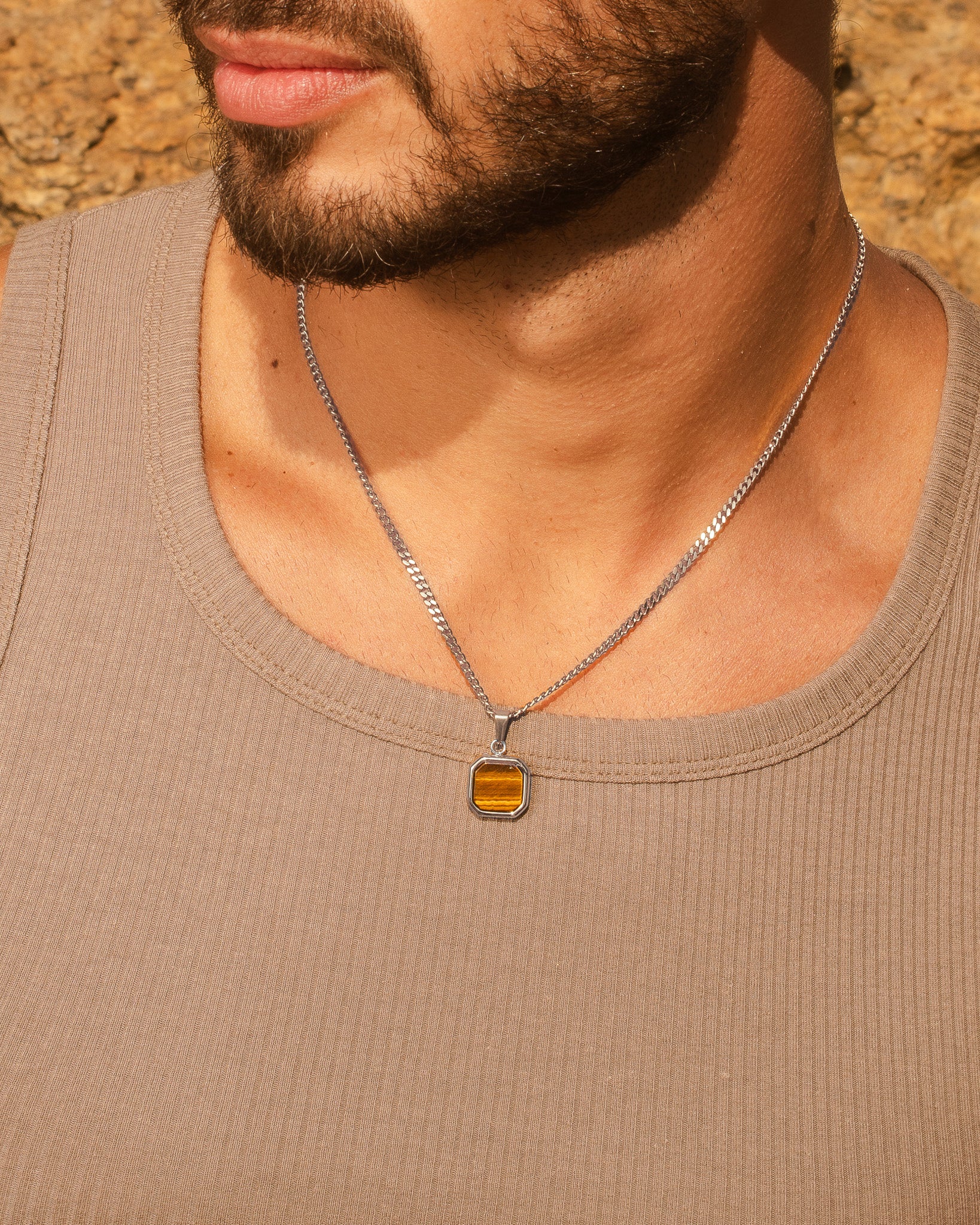 Collares dorados en capas sobre camisa marrón con colgante cuadrado ámbar y charm de cruz.