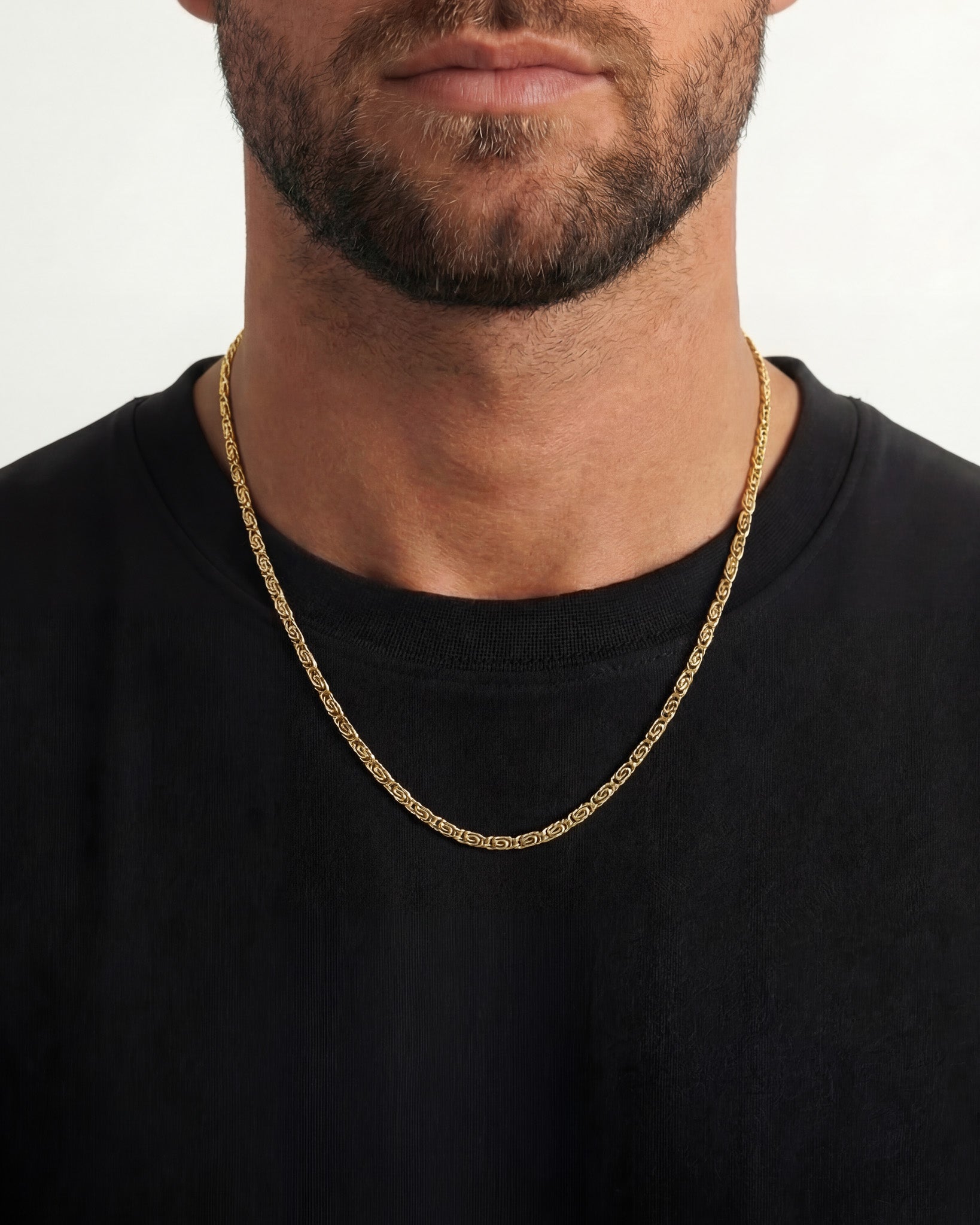 Man wearing two gold chain necklaces around the neck shown from the chest up with a black shirt
