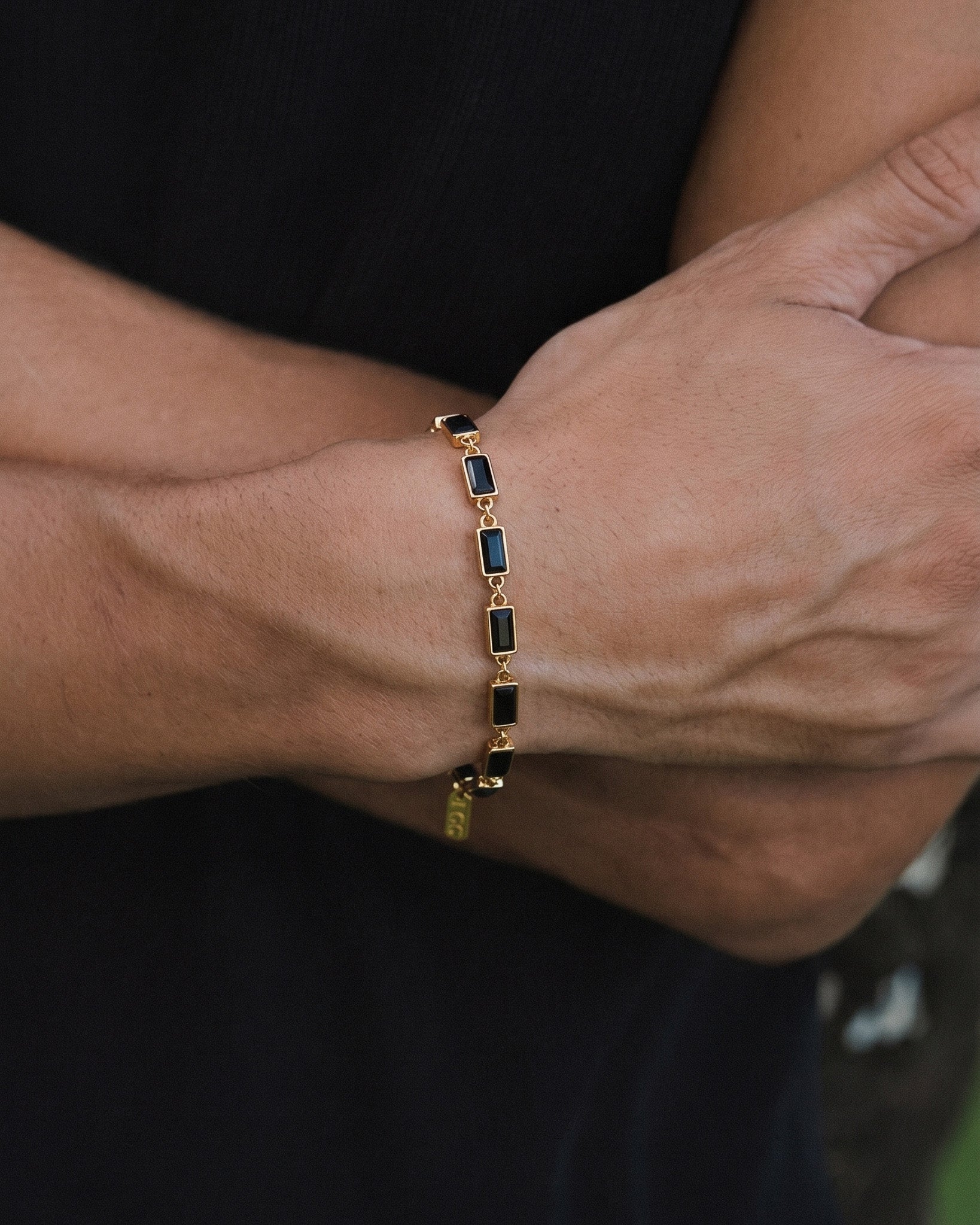 Pulsera dorada Omen con piedras rectangulares oscuras enlazadas en la muñeca