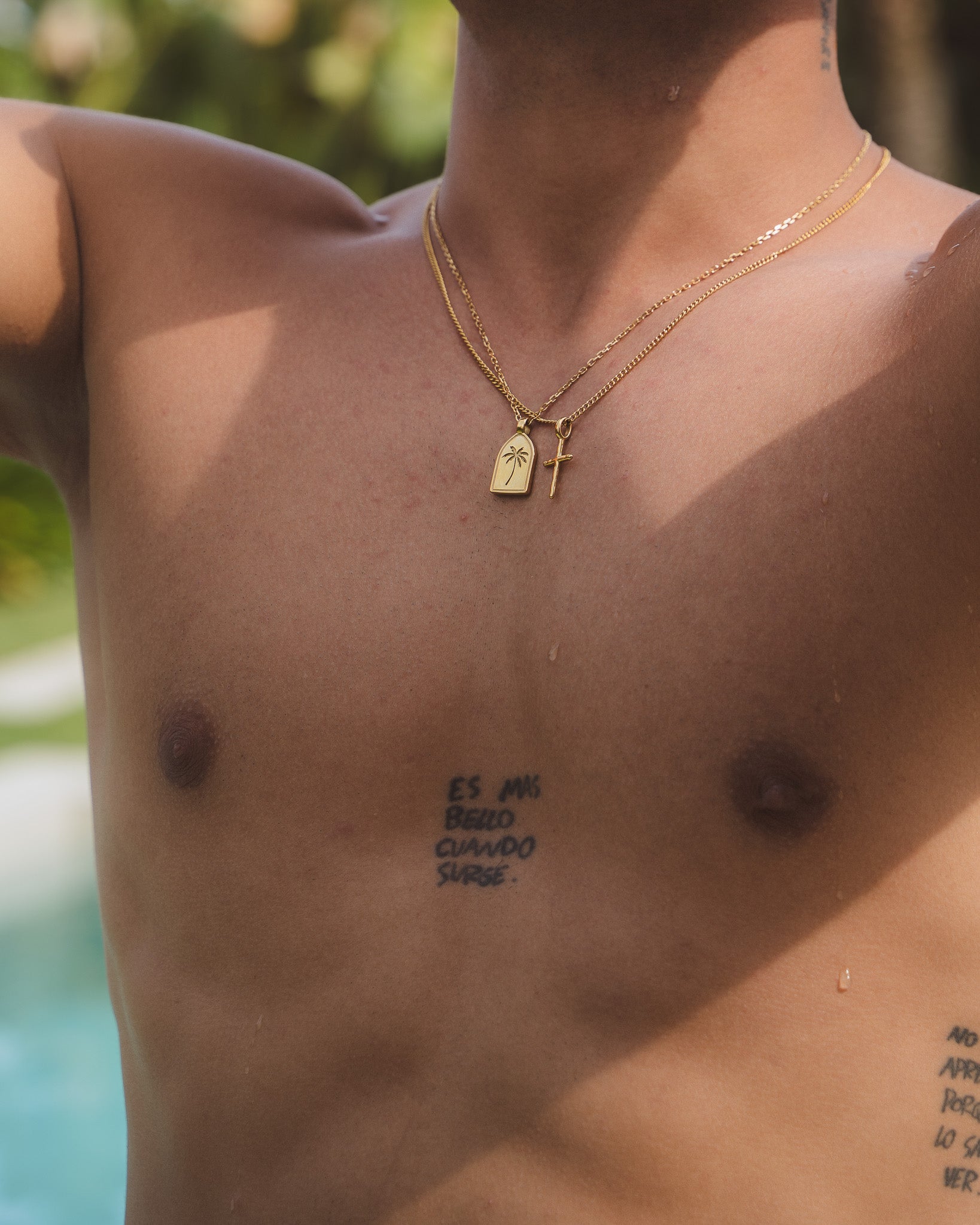 Model wearing layered gold necklaces with palm tree and cross pendants