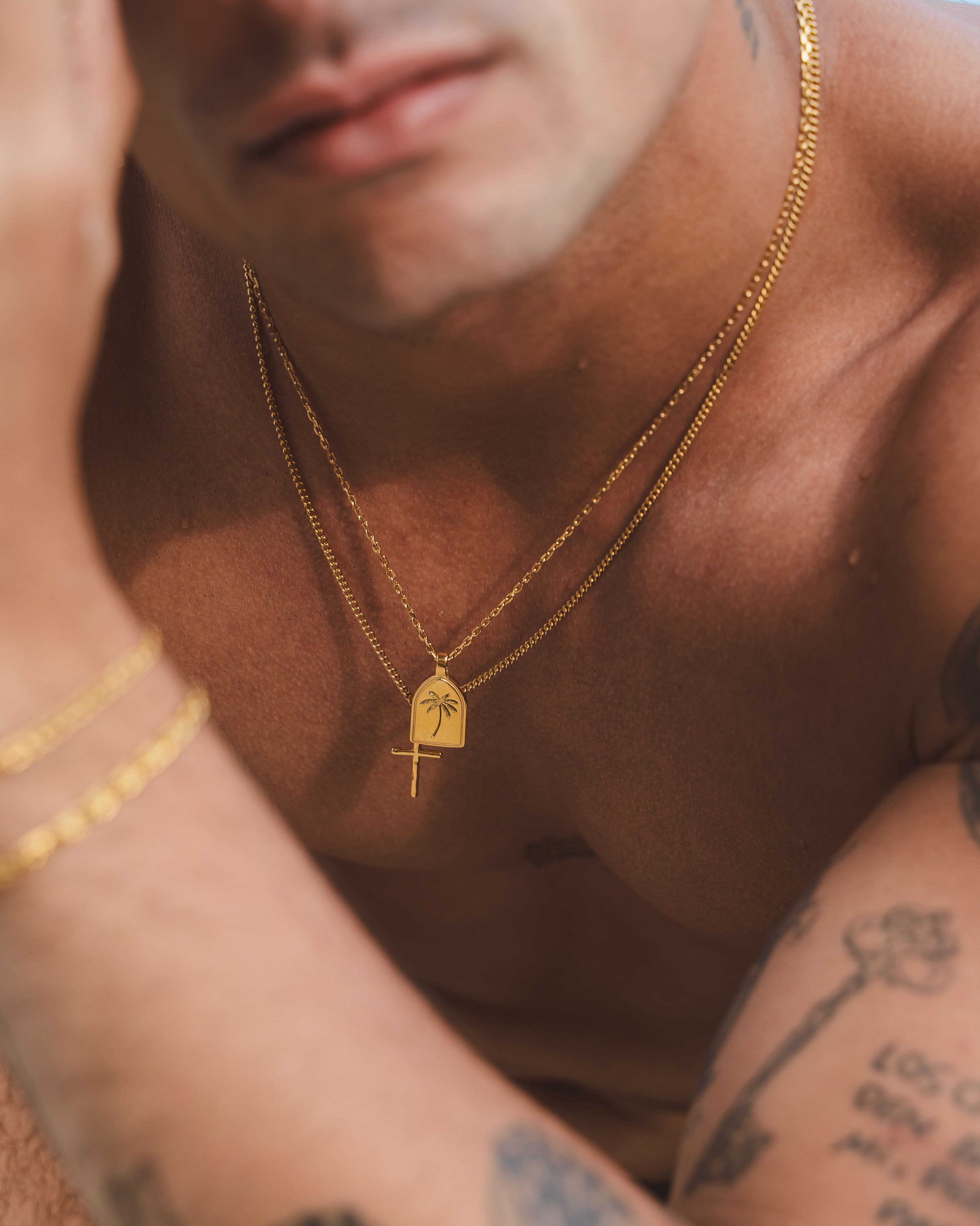 Layered gold necklaces featuring a palm tree pendant and a cross charm on the chest