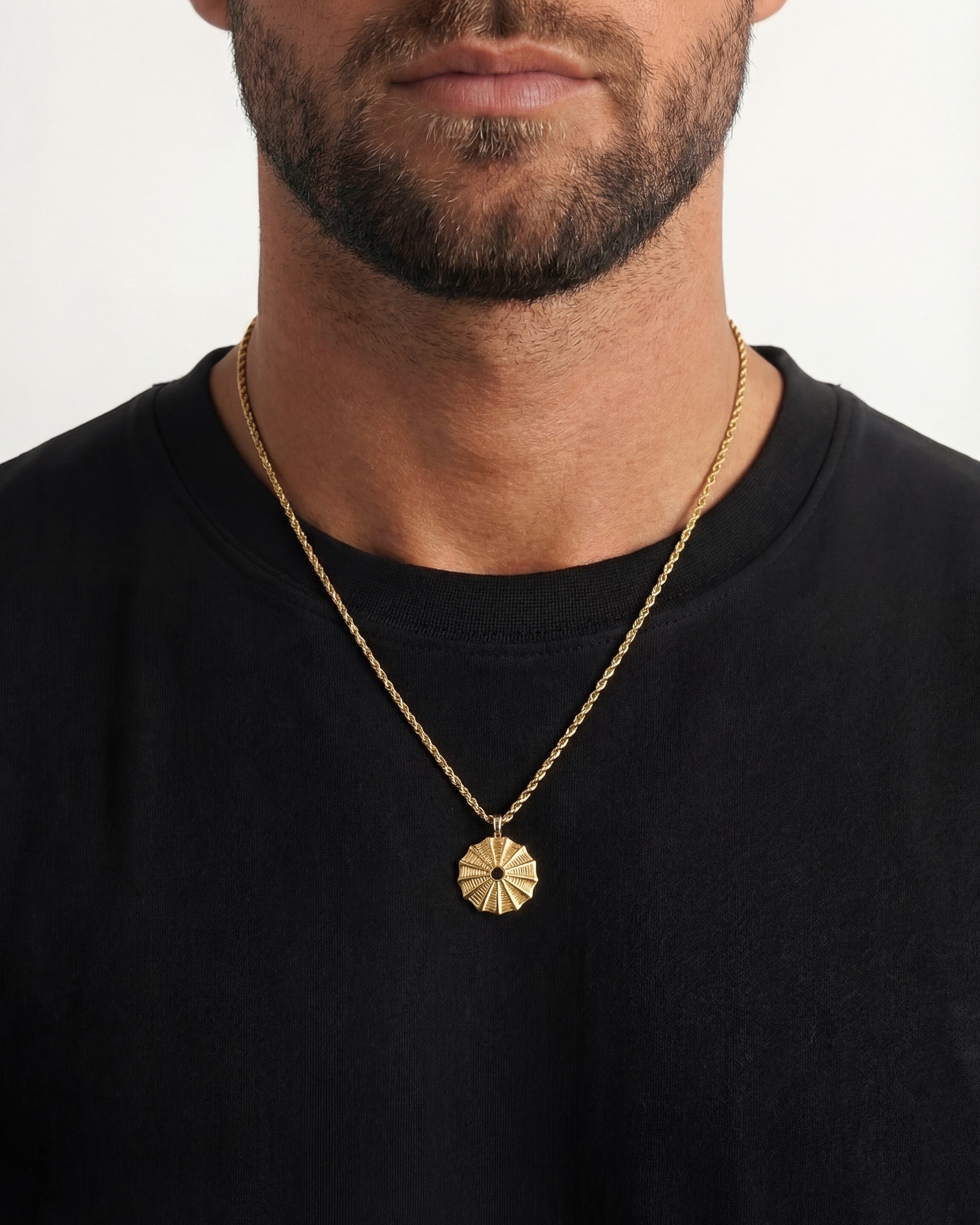 Gold sunburst pendant necklace worn by a man on a black shirt.