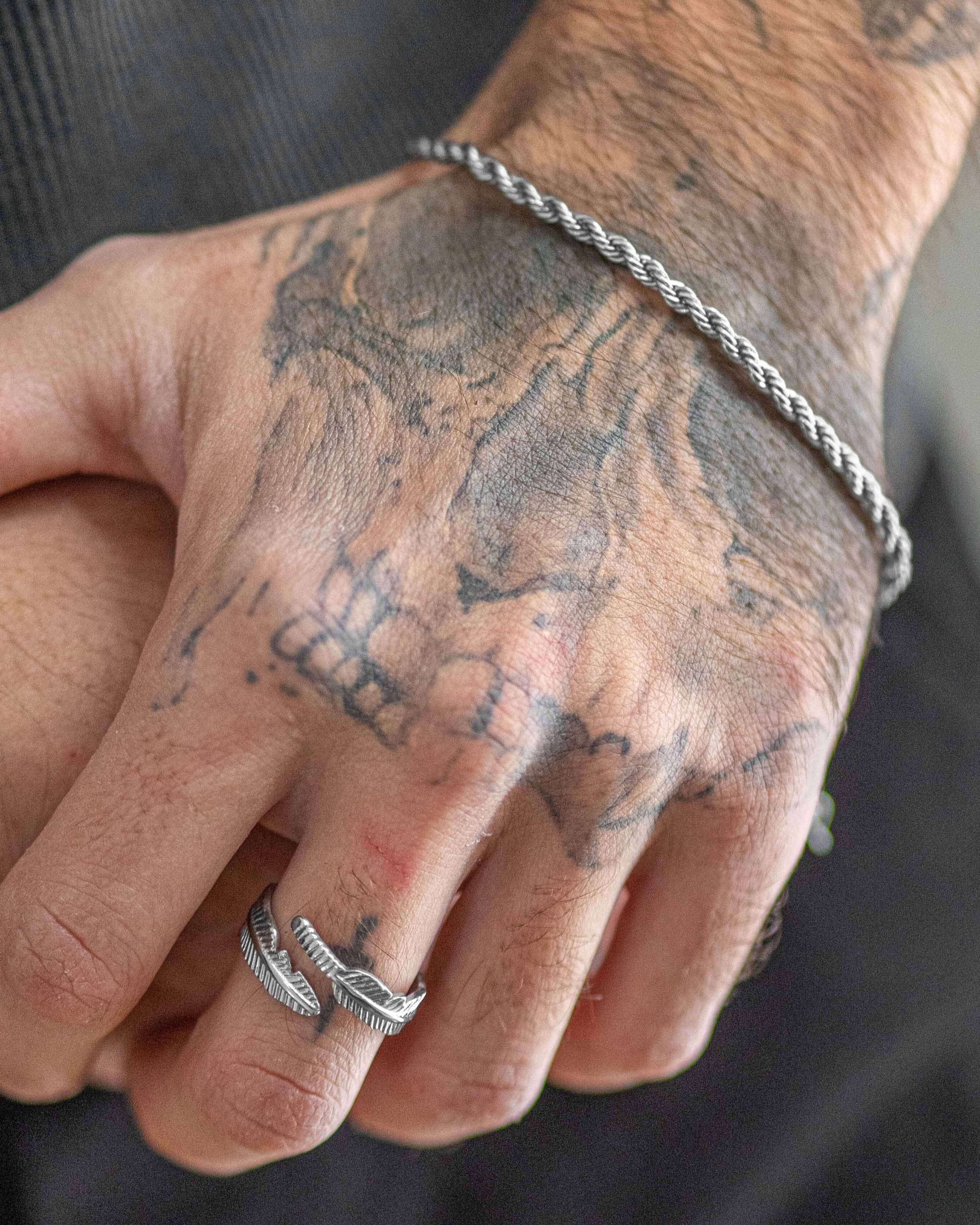 Anillo plateado minimalista Tahoe en un dedo con tatuajes visibles en la mano